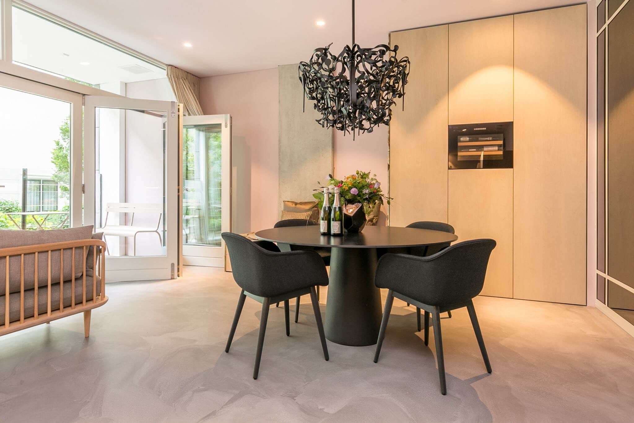 Round dining table with dark chairs under a sculptural black chandelier
