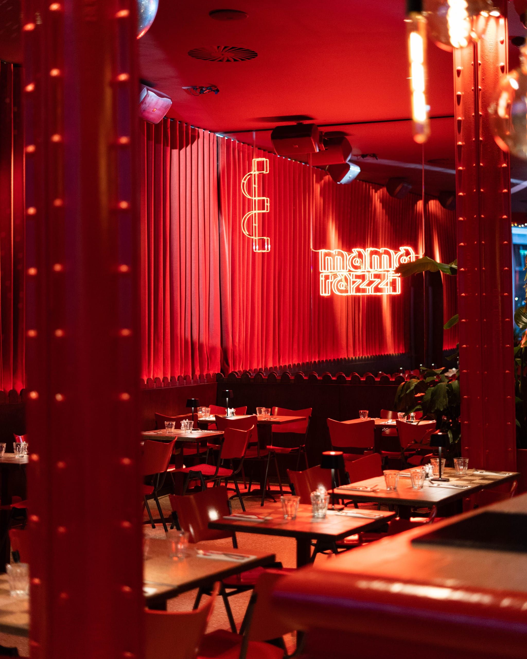 Studded red columns and pleated curtains behind the neon sign at Mamarazzi