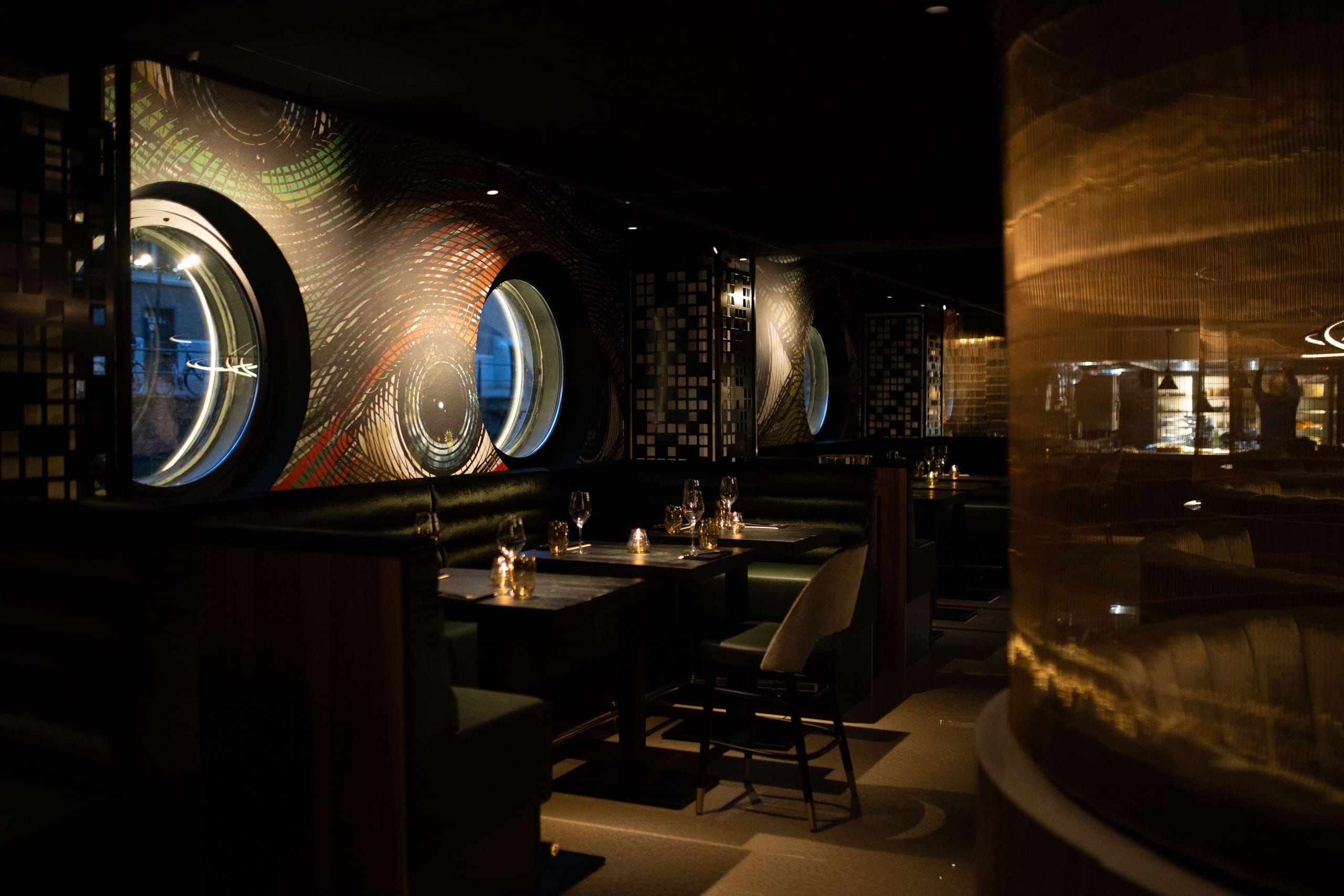 Porthole windows and graphic wall murals above dark booths at Vandal