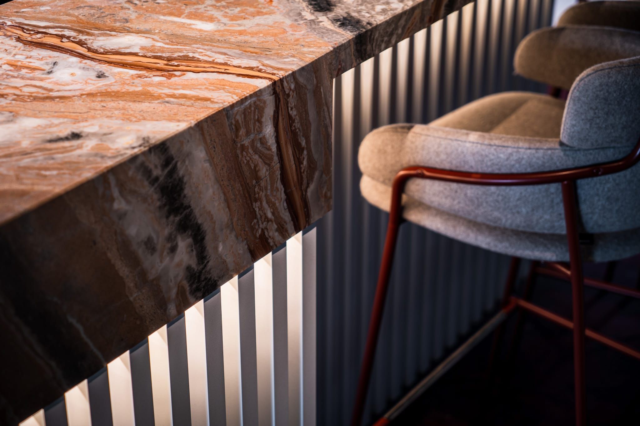 Close-up of a marble bar top over a fluted front with a grey bar stool