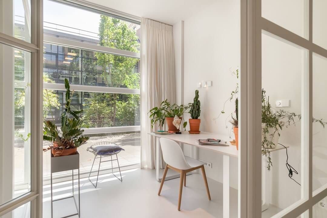 Home office with white desk and chair beside a tall courtyard window