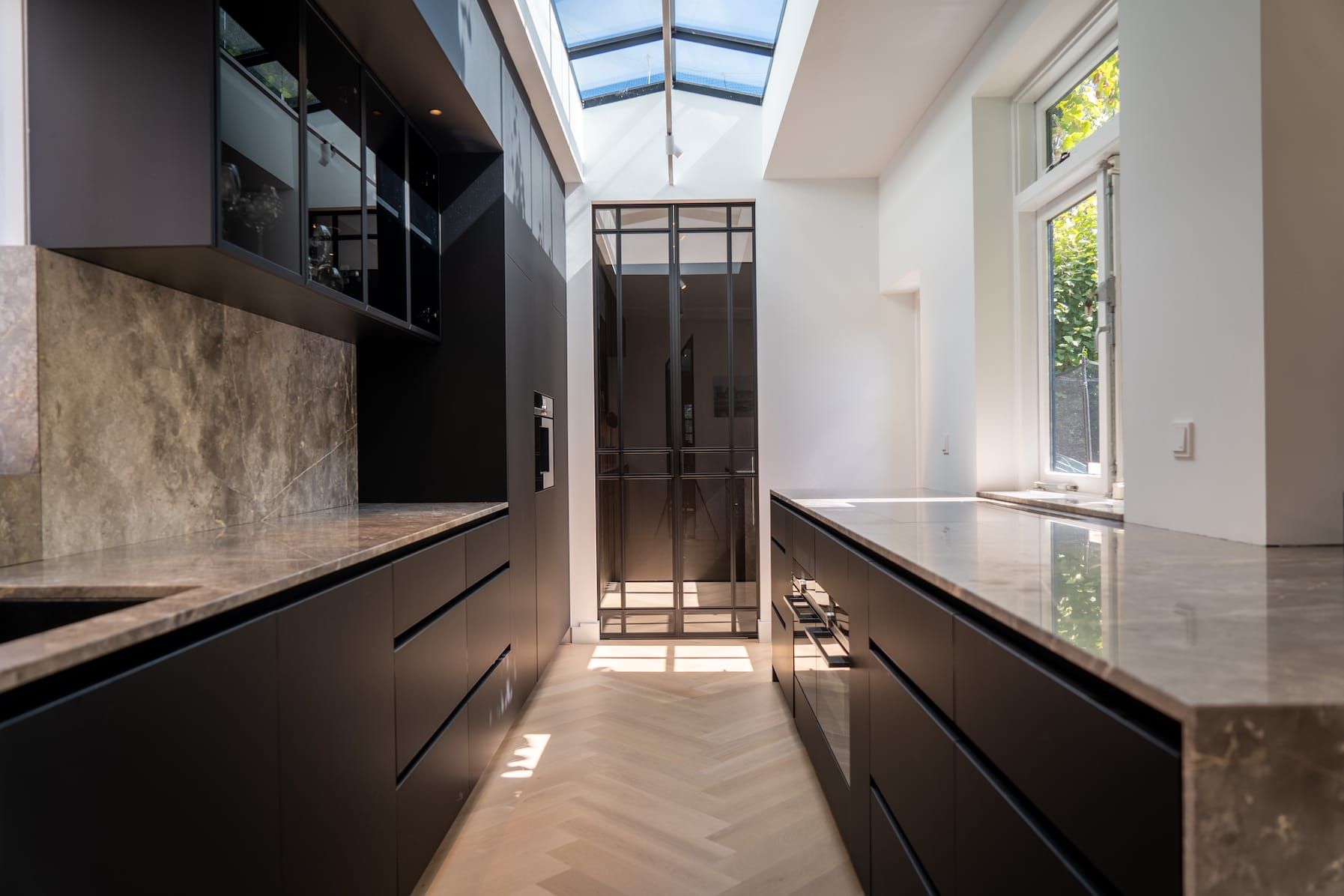 Narrow kitchen with black cabinetry, stone worktops, skylight and herringbone floor