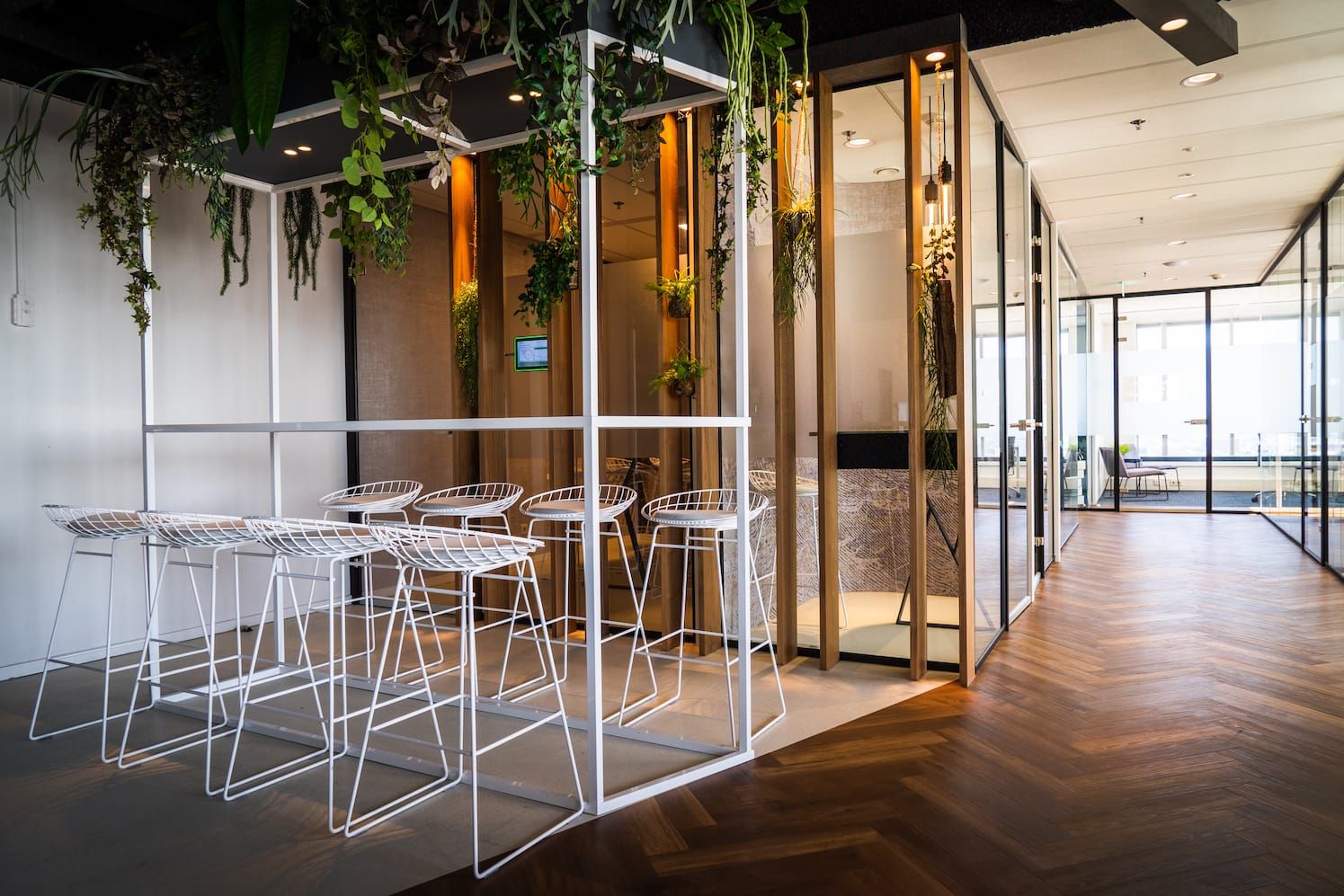 White wire stools at a framed high table with hanging plants beside glass rooms
