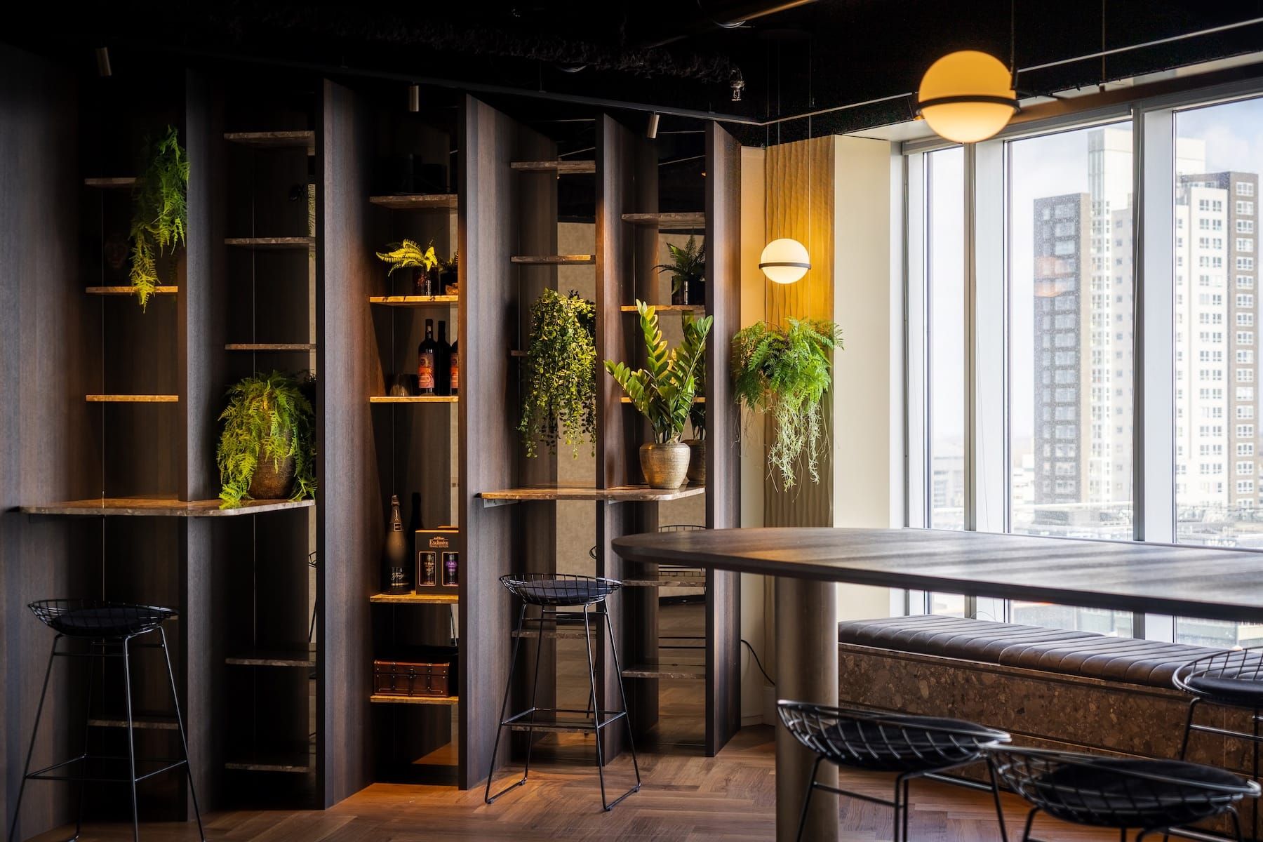 Dark oak shelving with ferns, bottles and a round pendant beside a bar table