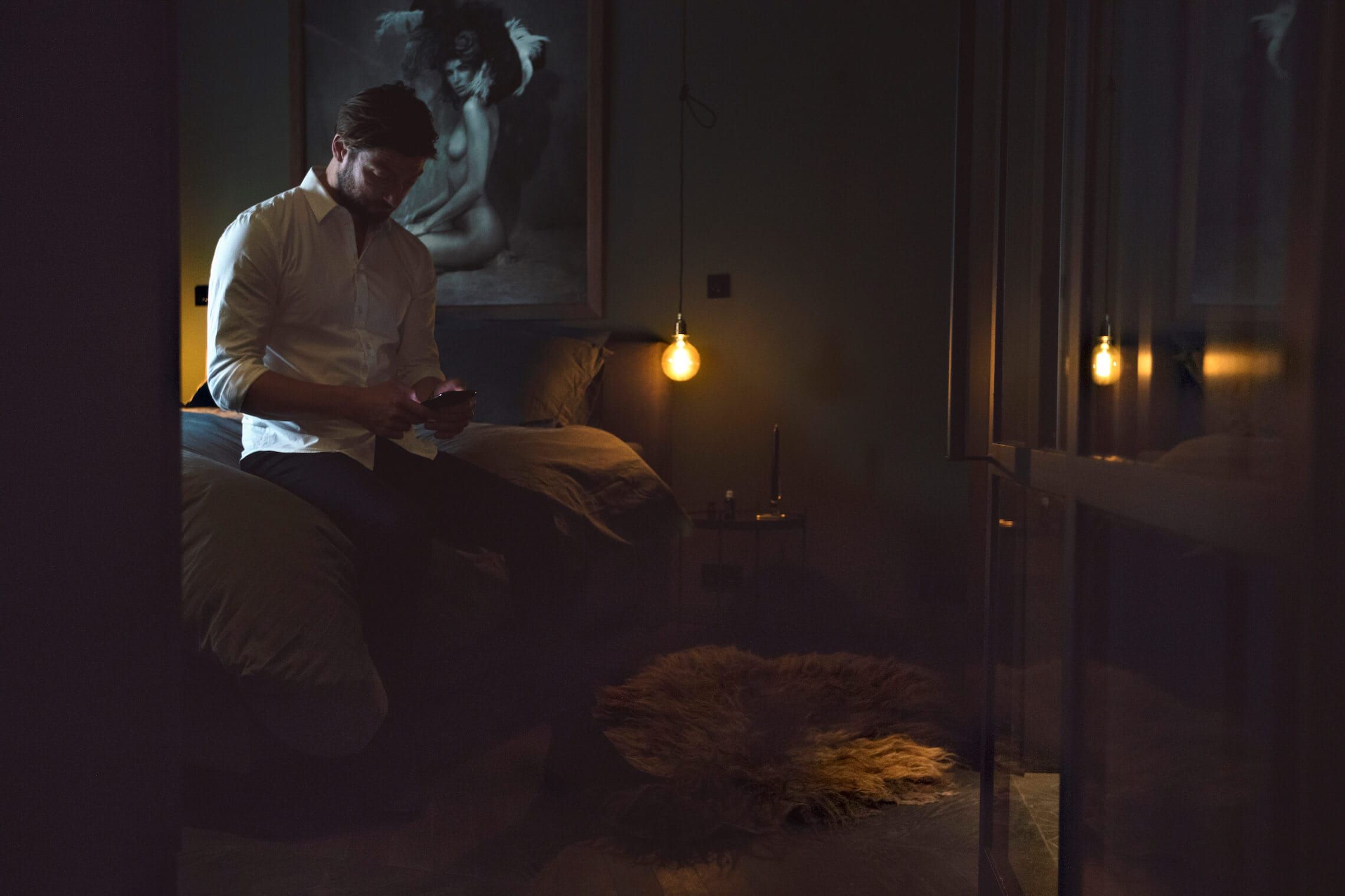 Bedroom in low light with a pendant bulb, sheepskin rug and artwork on the wall