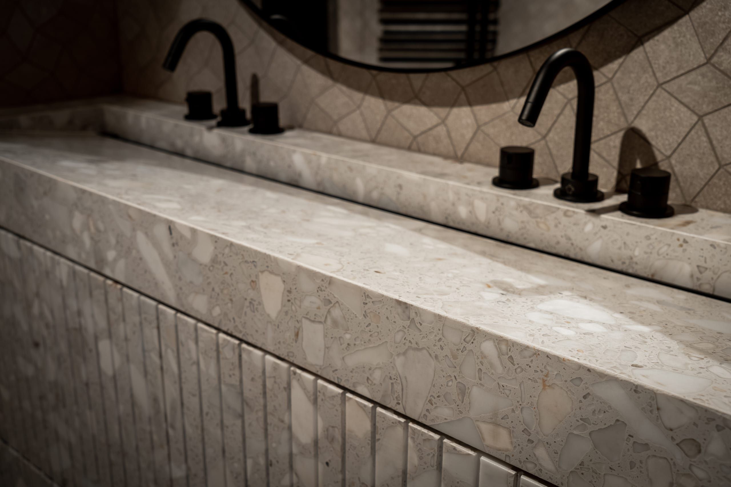 Terrazzo vanity top with matt black taps below a round mirror