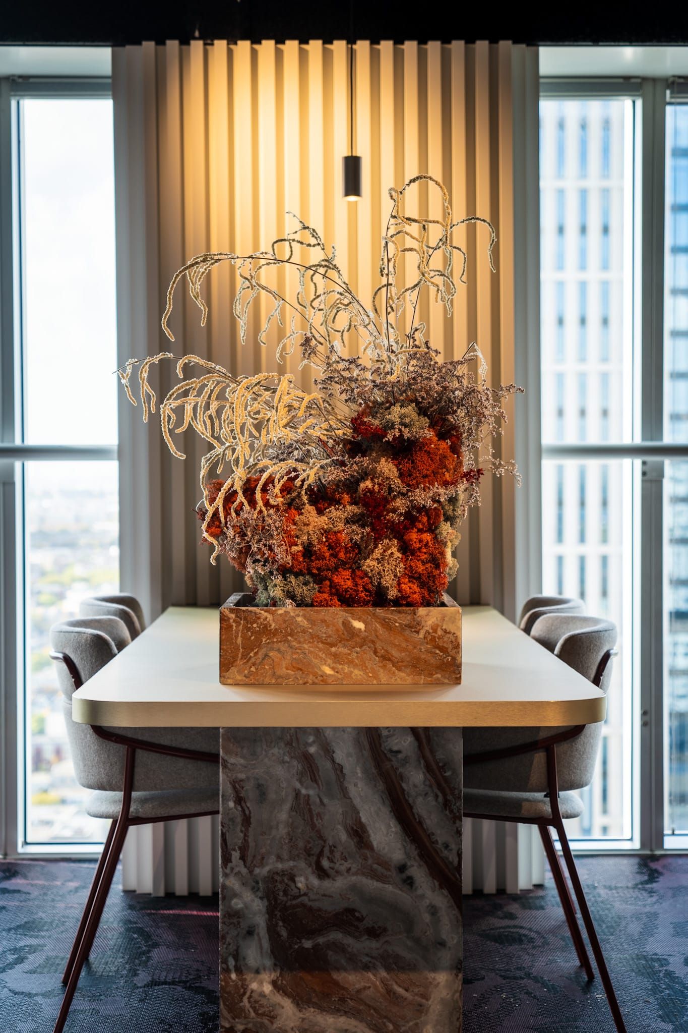 Marble dining table with dried flower arrangement before a fluted window wall