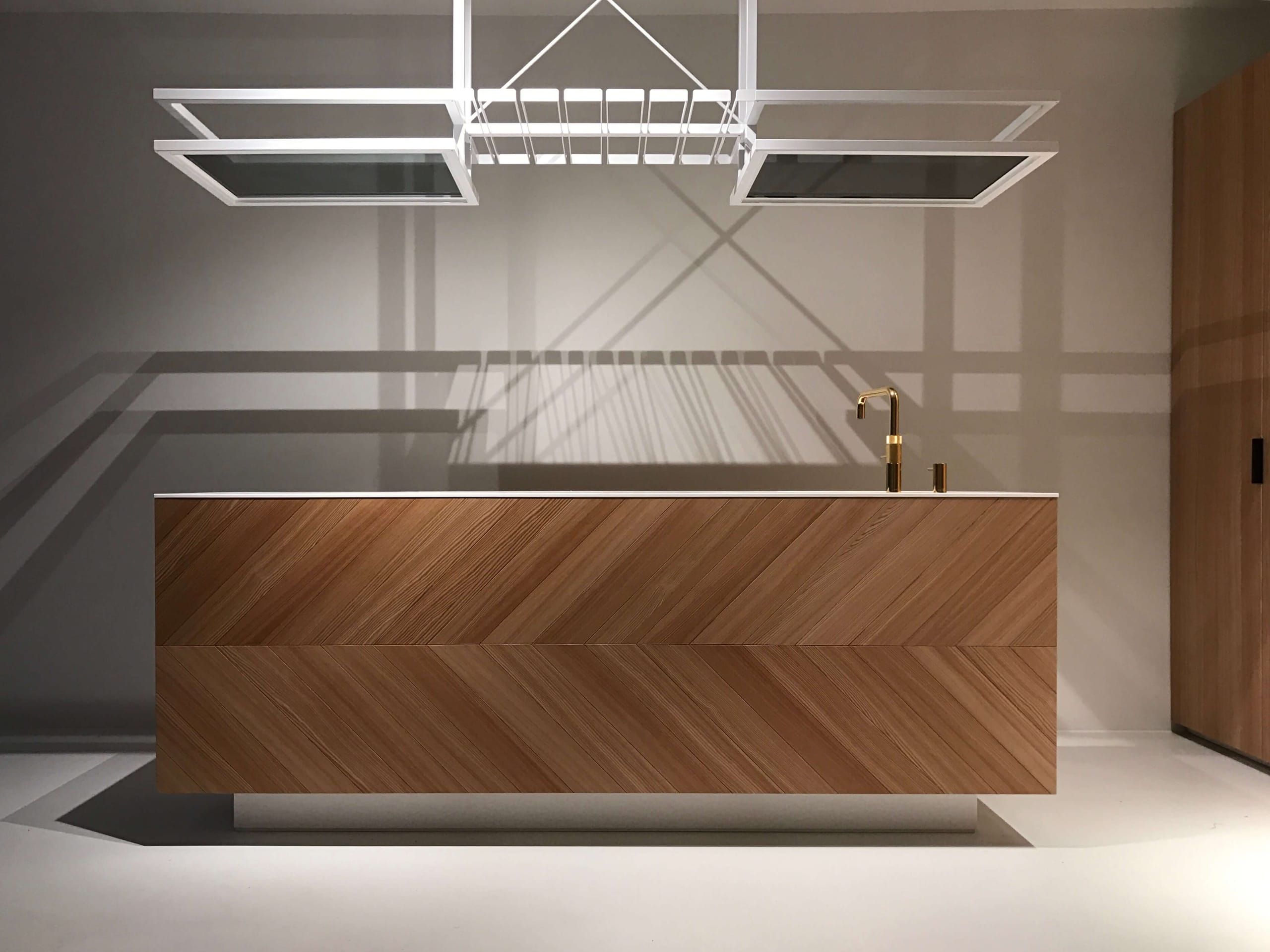 Oak herringbone kitchen island with brass tap under a white hanging glass rack