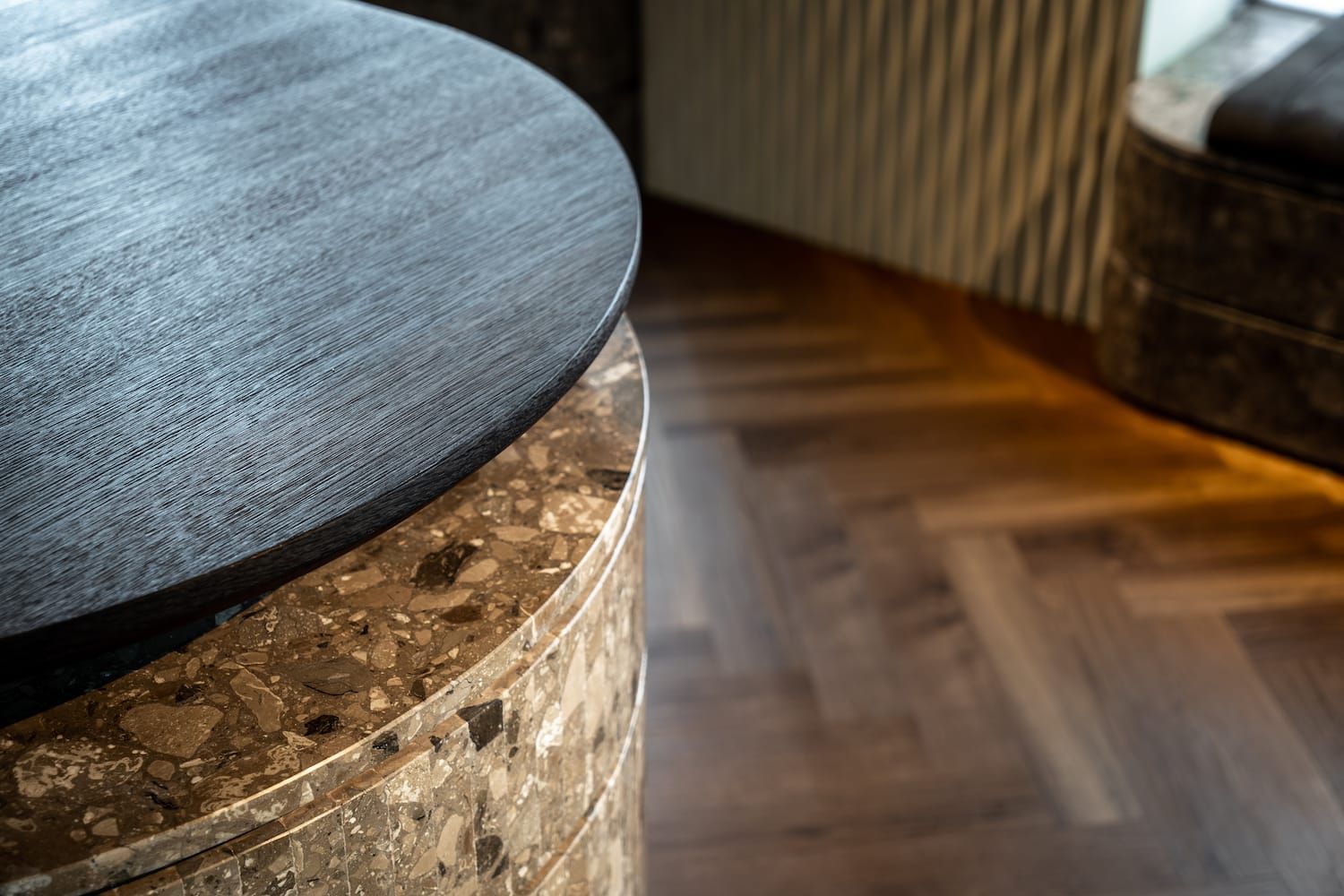 Close-up of a black oak tabletop on a terrazzo base above herringbone flooring
