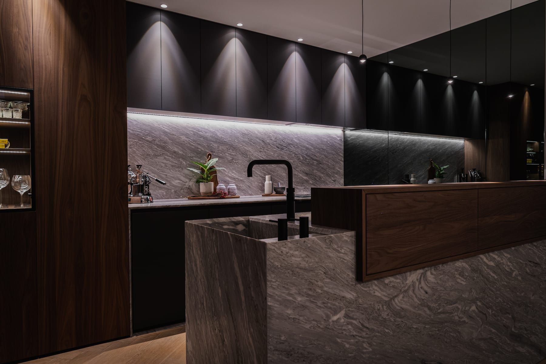 Marble kitchen island with sink below black cabinets and a stone backsplash