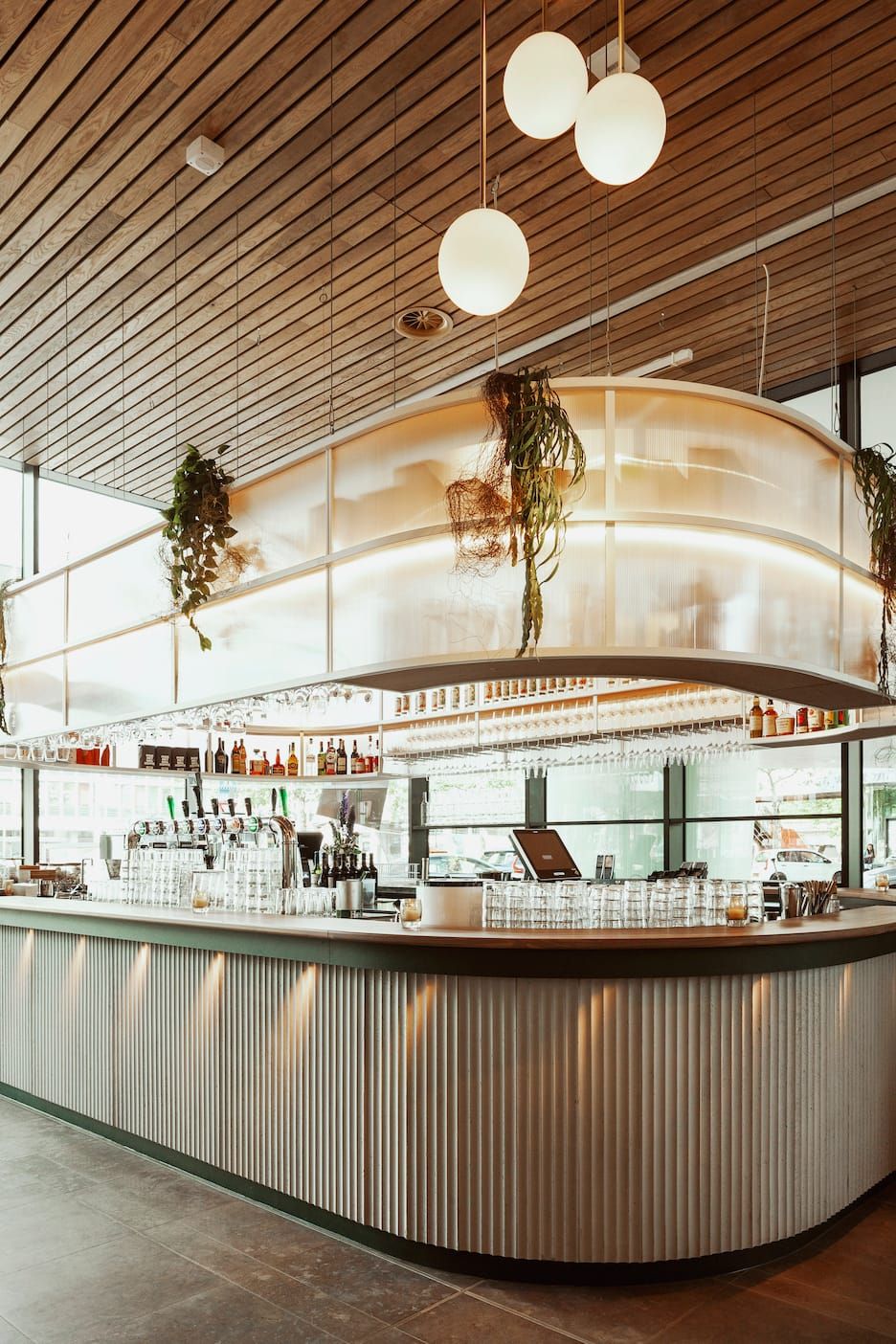 Curved bar with fluted front and frosted canopy under globe pendants at Fontein