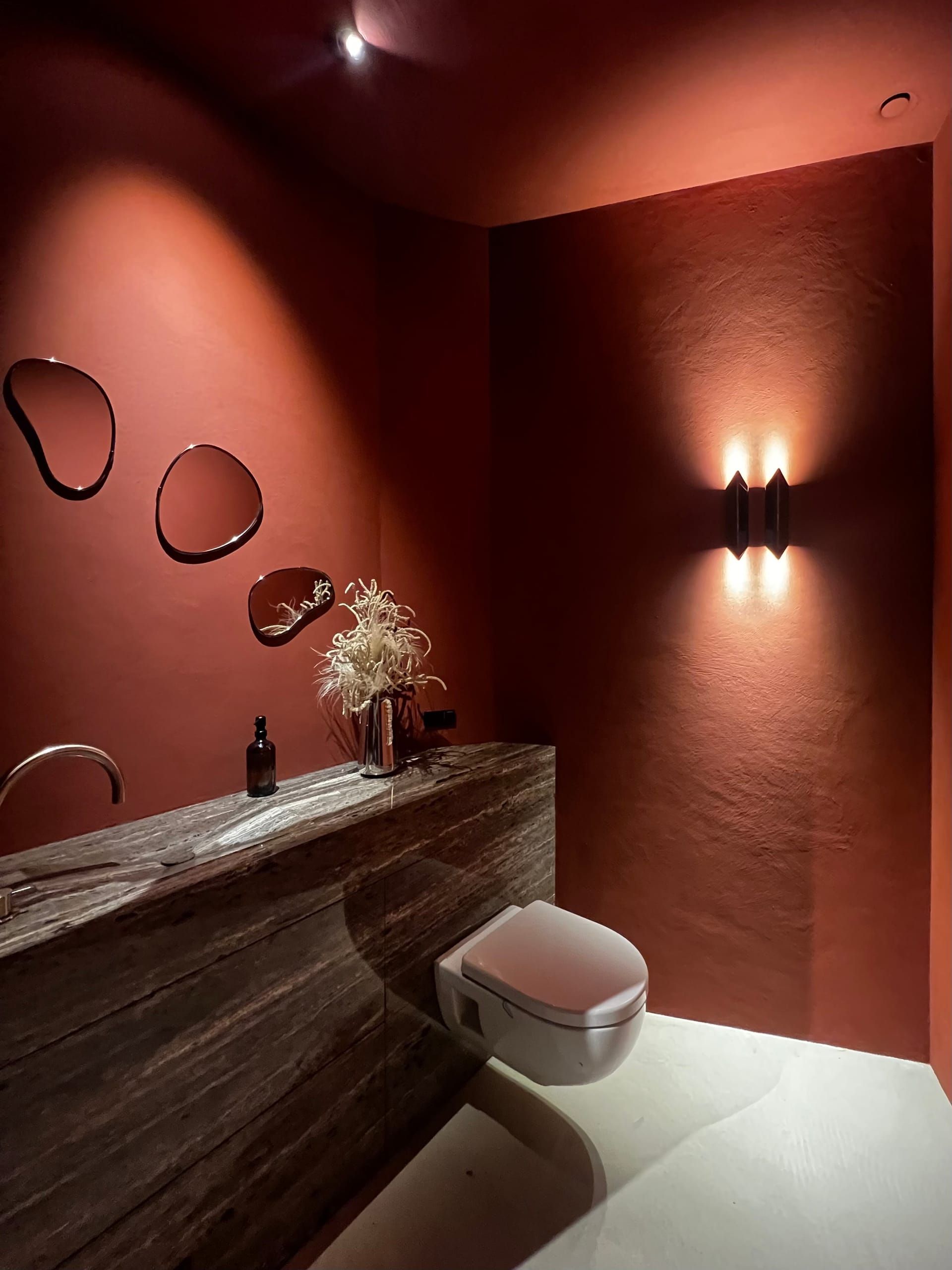 Terracotta powder room with wall lights, organic mirrors and a stone washbasin counter