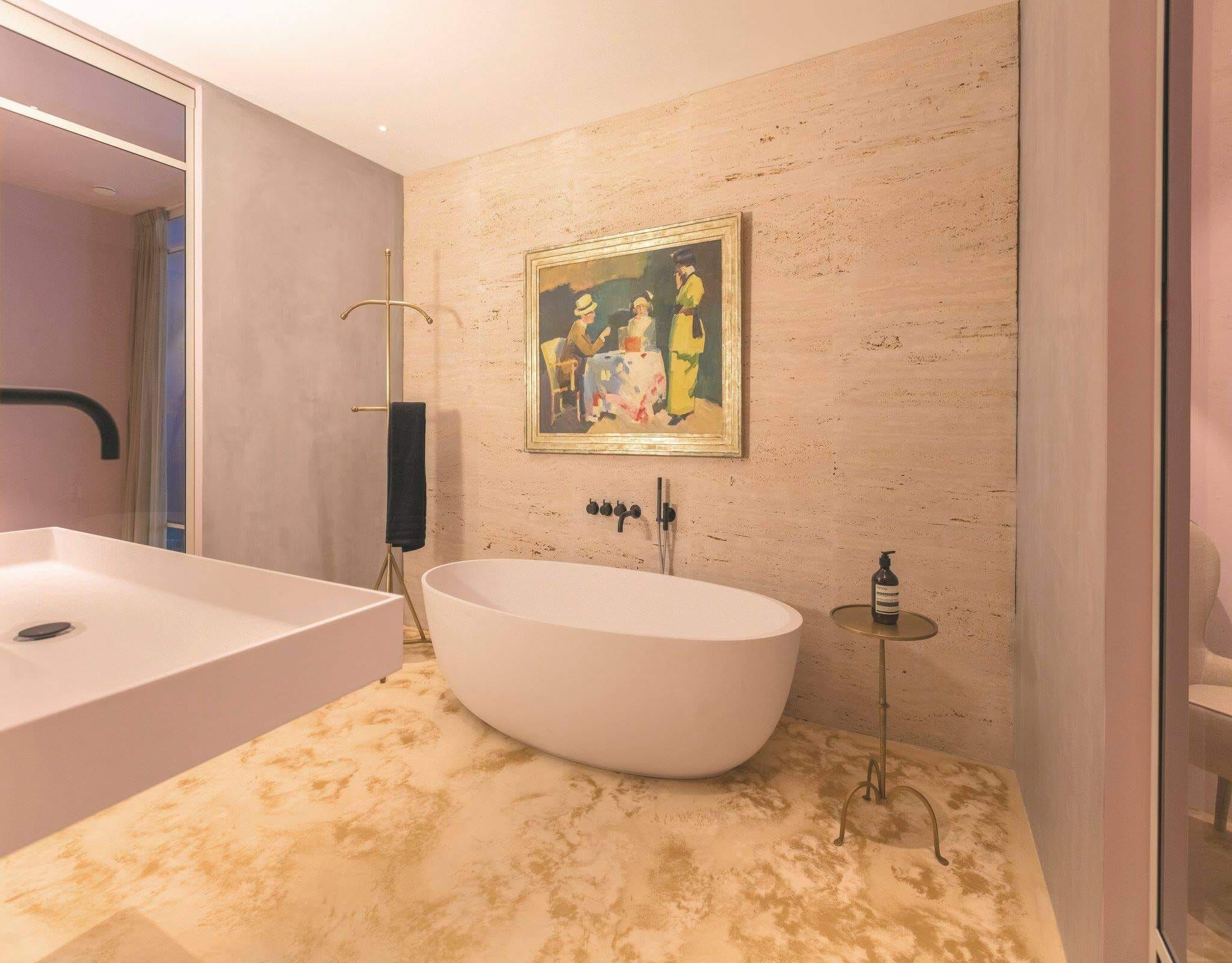 Freestanding white bath on a travertine wall with a framed painting in Stardust