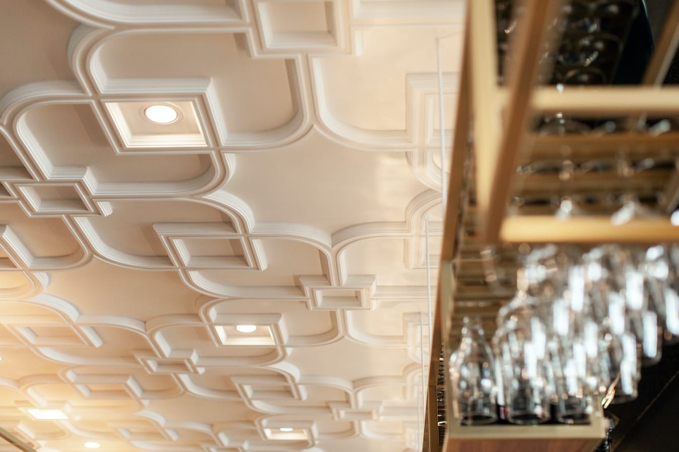 Ornate plaster ceiling with recessed lights above bar glass racks