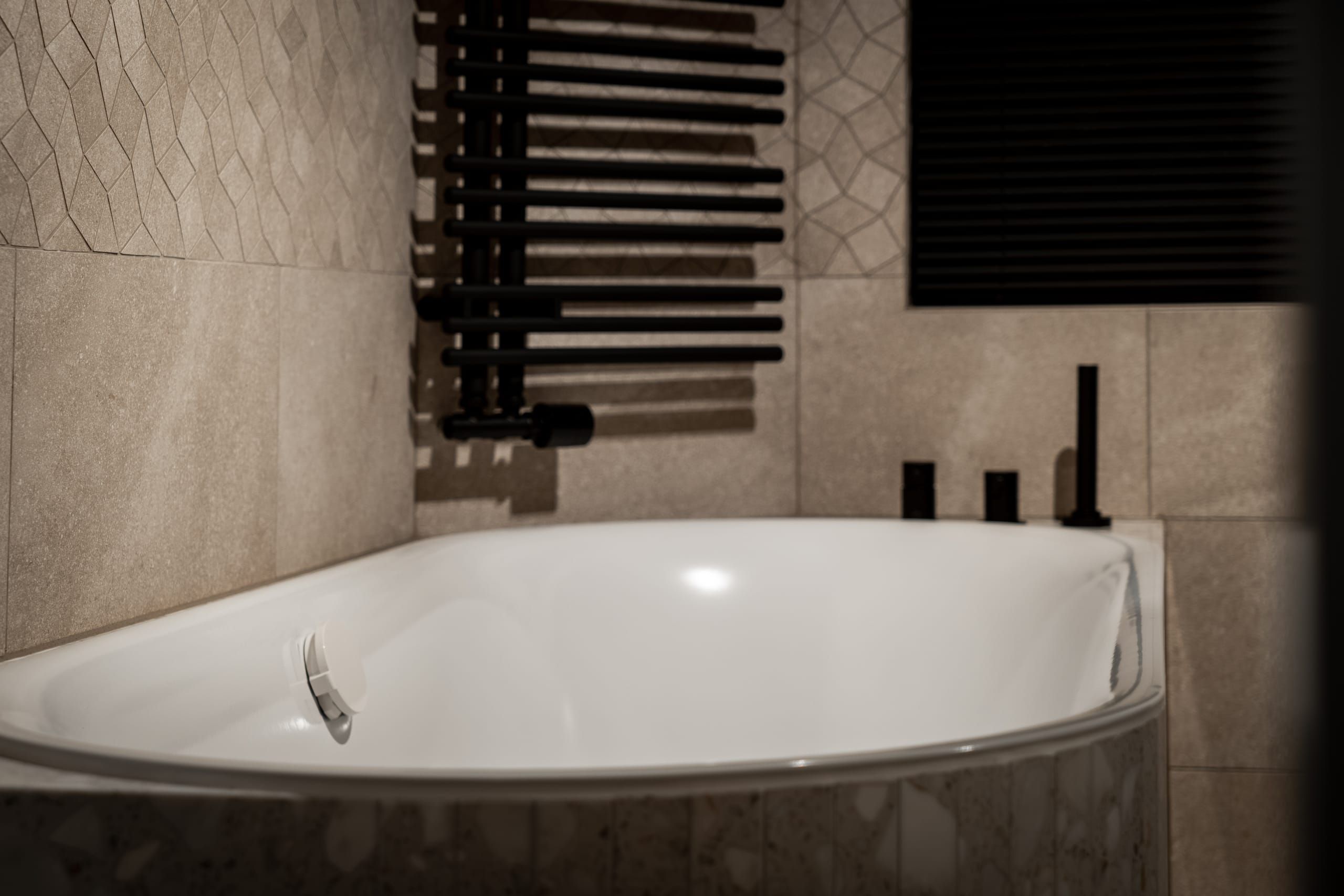Matt black radiator and white bath beside patterned wall tiles