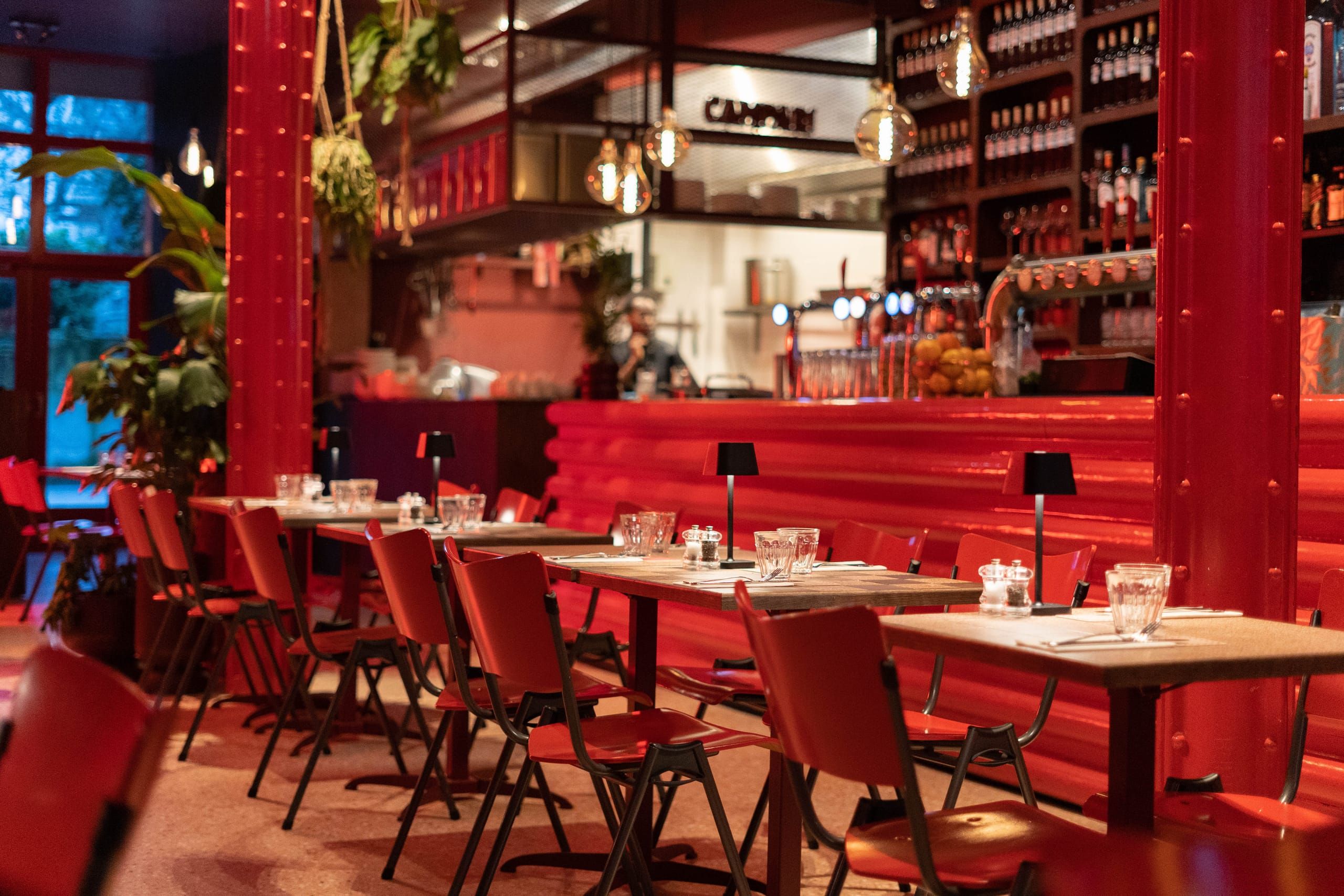 Red lacquered bar with shelves of bottles and black table lamps at Mamarazzi