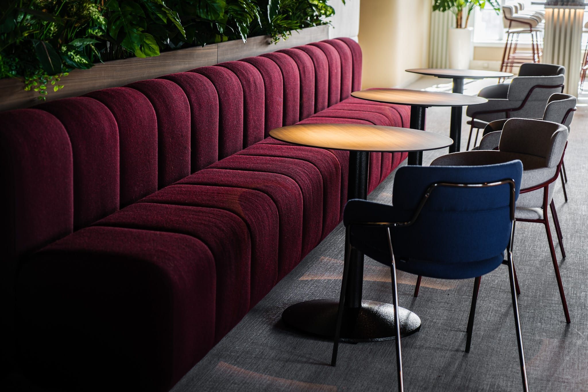 Burgundy ribbed banquette with round tables and blue and grey armchairs