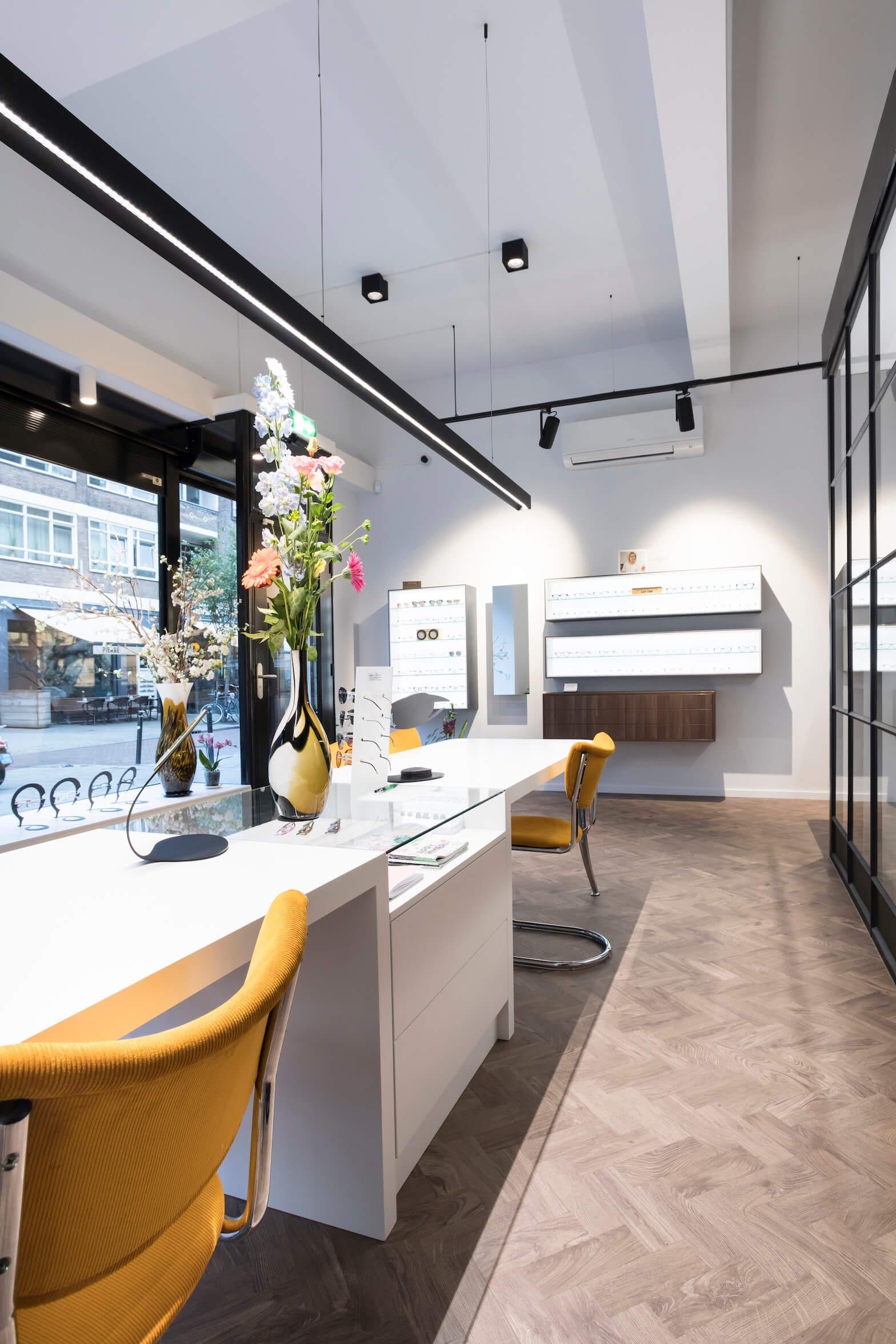 Glass display counter with flowers and yellow chairs looking toward the street window