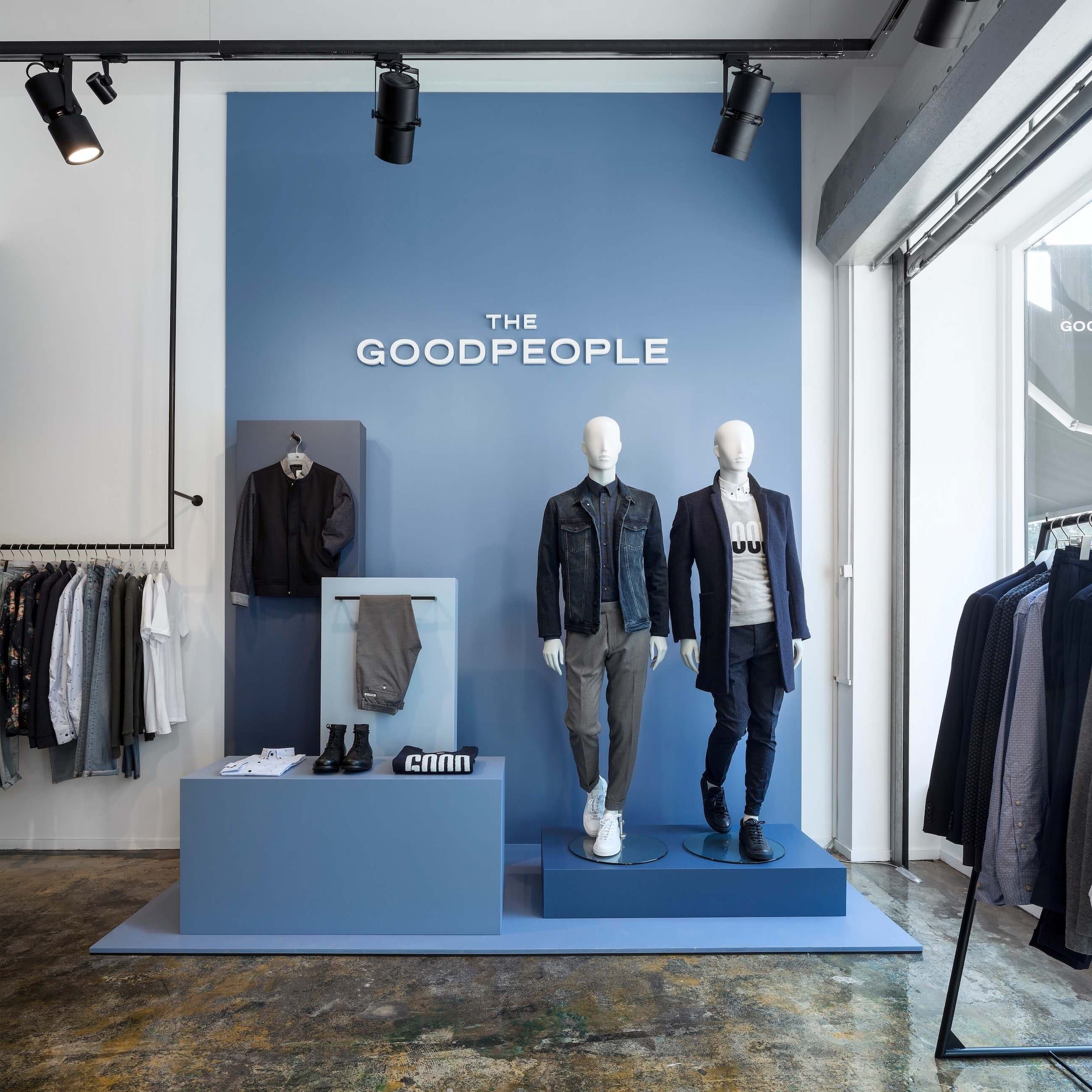 Blue display wall with mannequins, shoes and folded knitwear on stepped blue plinths