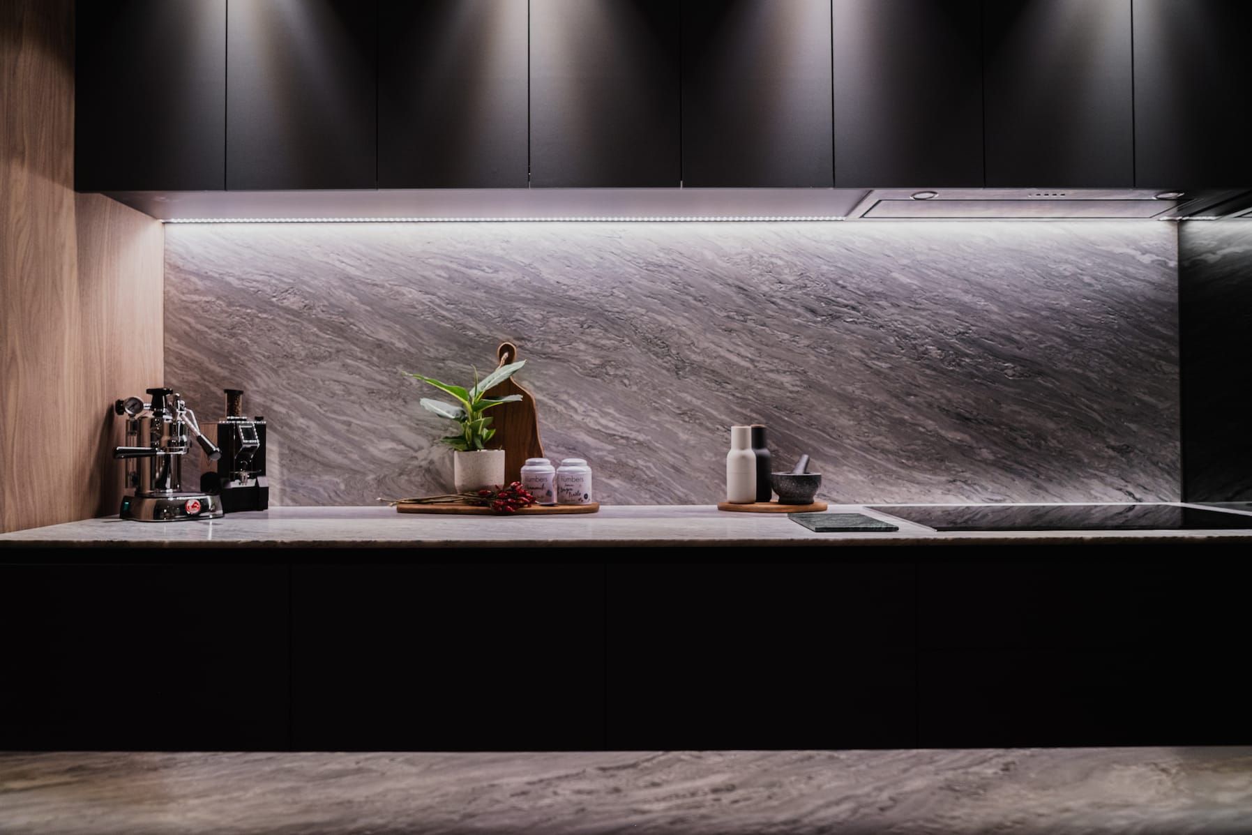 Stone backsplash with LED strip light above a black kitchen counter