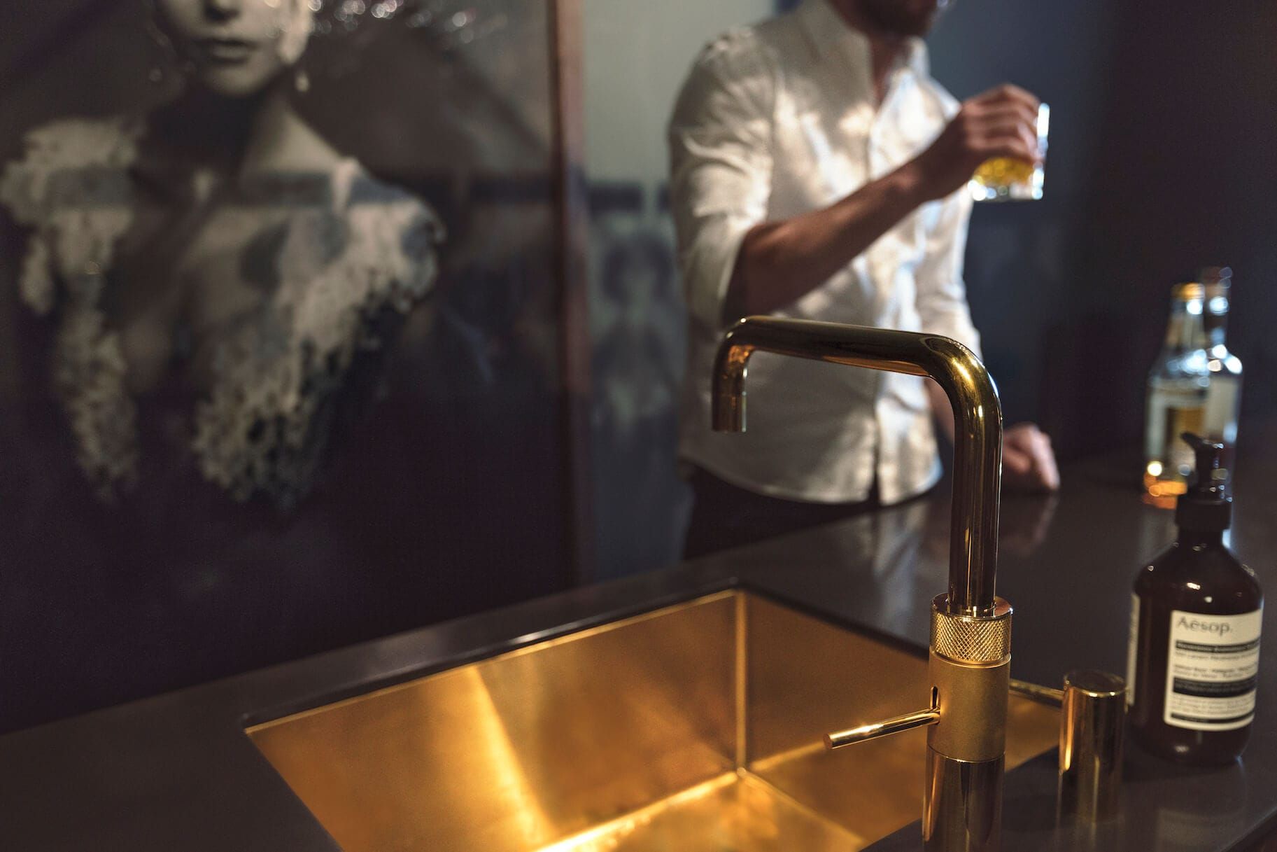 Brass tap and sink in a dark worktop with an artwork behind