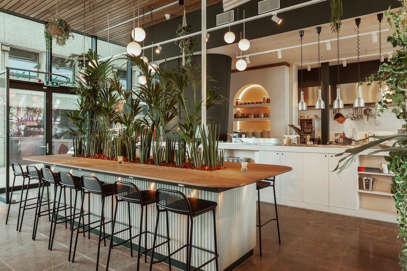 Planted wooden bar counter with black stools and open kitchen at Fontein