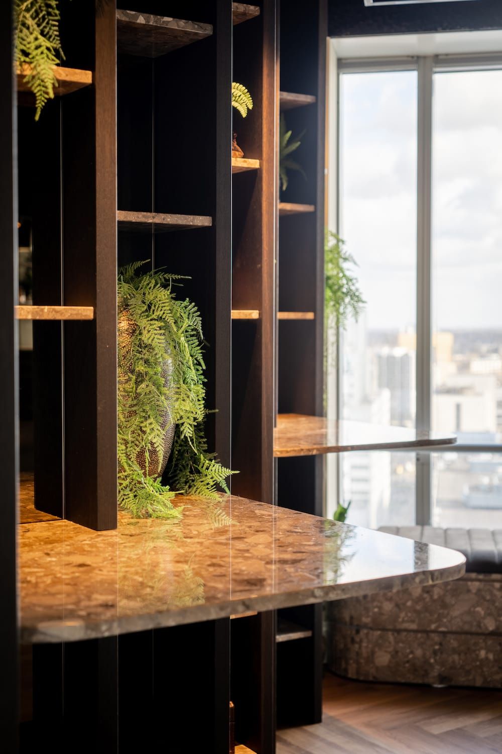 Dark shelving with a fern in a vase and a terrazzo shelf top by the window