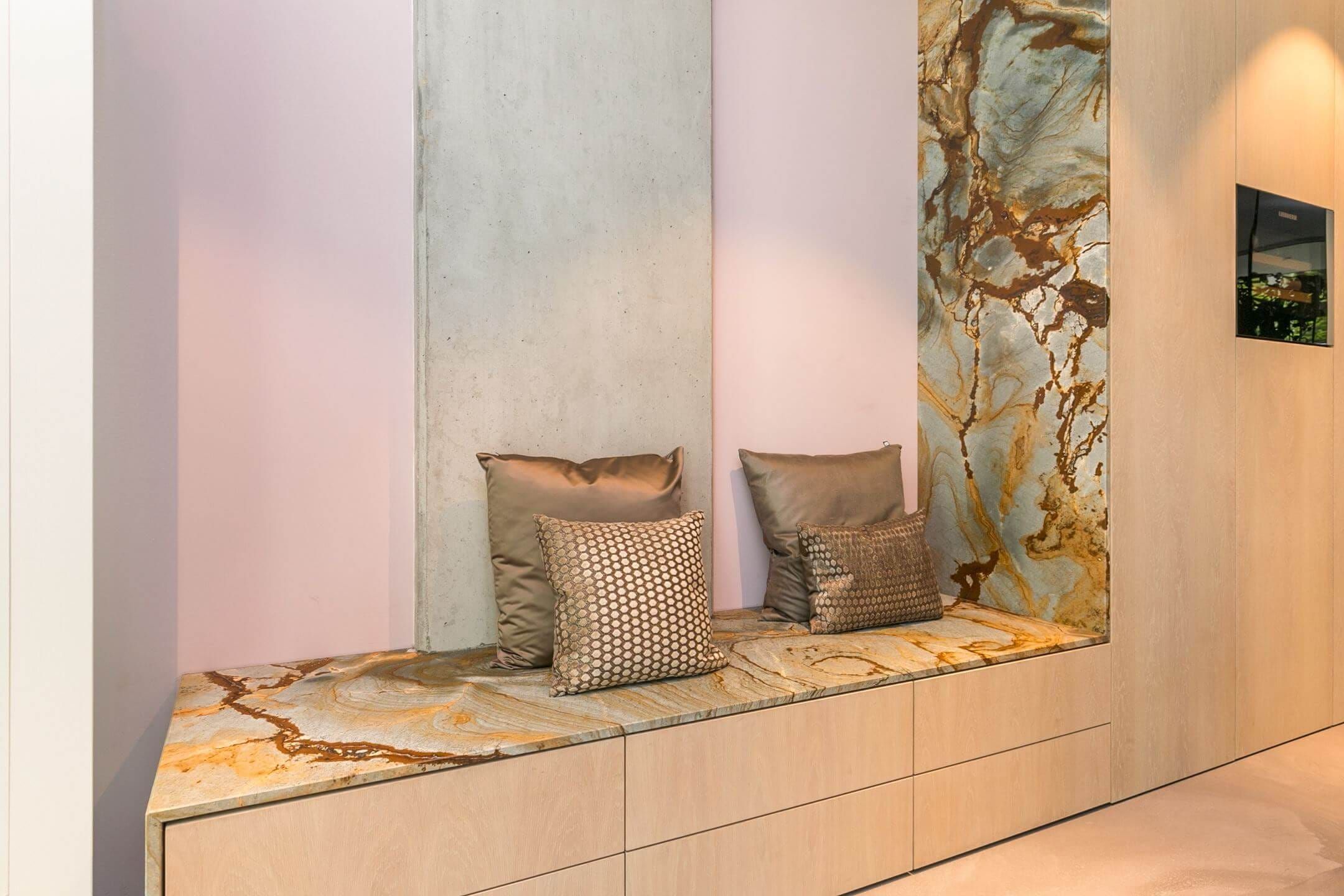 Built-in bench with colourful stone top and cushions beside a concrete column