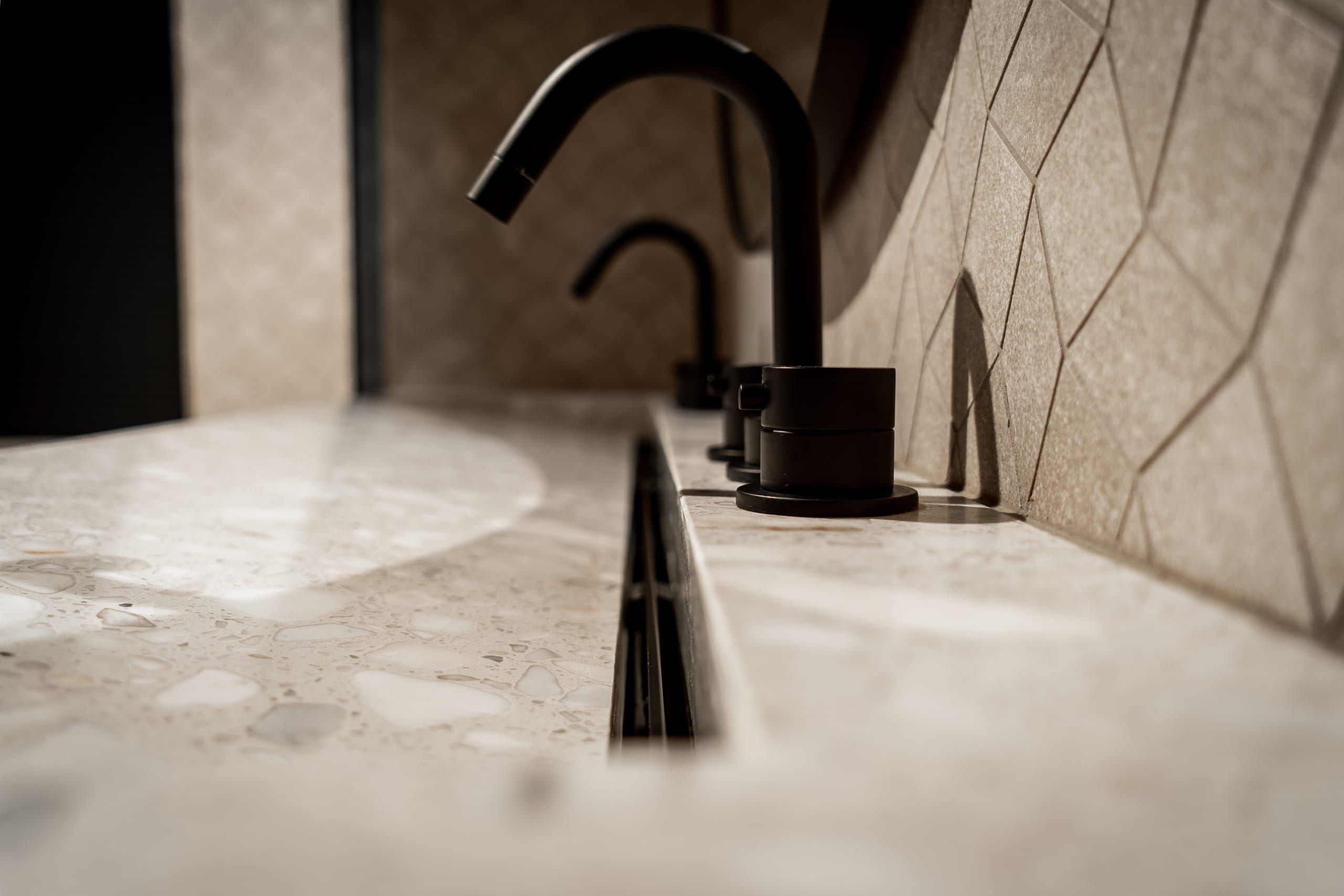 Matt black tap on the terrazzo basin ledge against geometric wall tiles