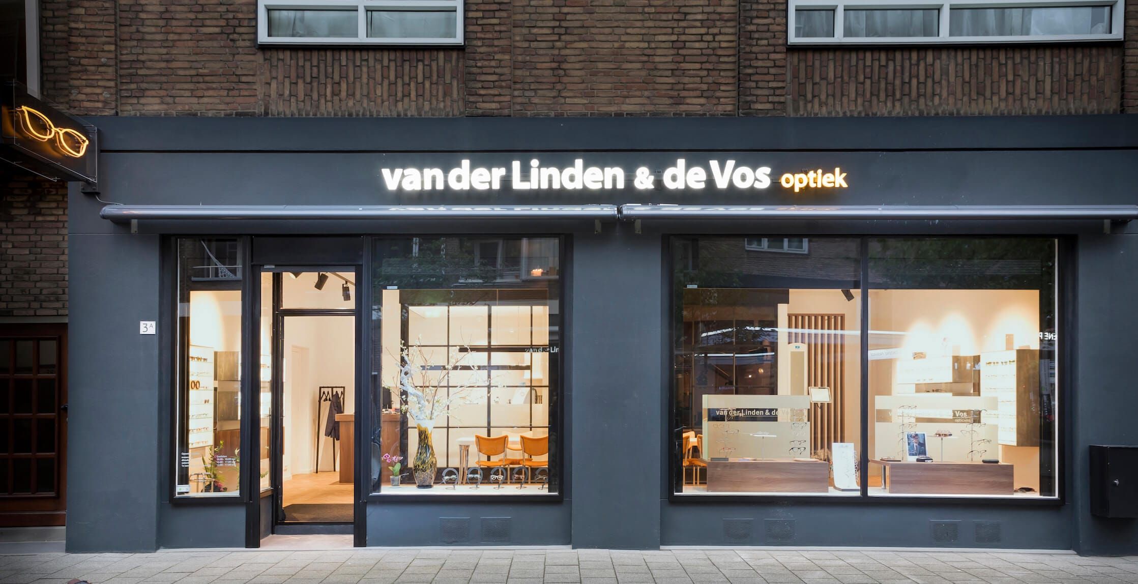 Shopfront of the optician with illuminated sign and a view into the warm interior