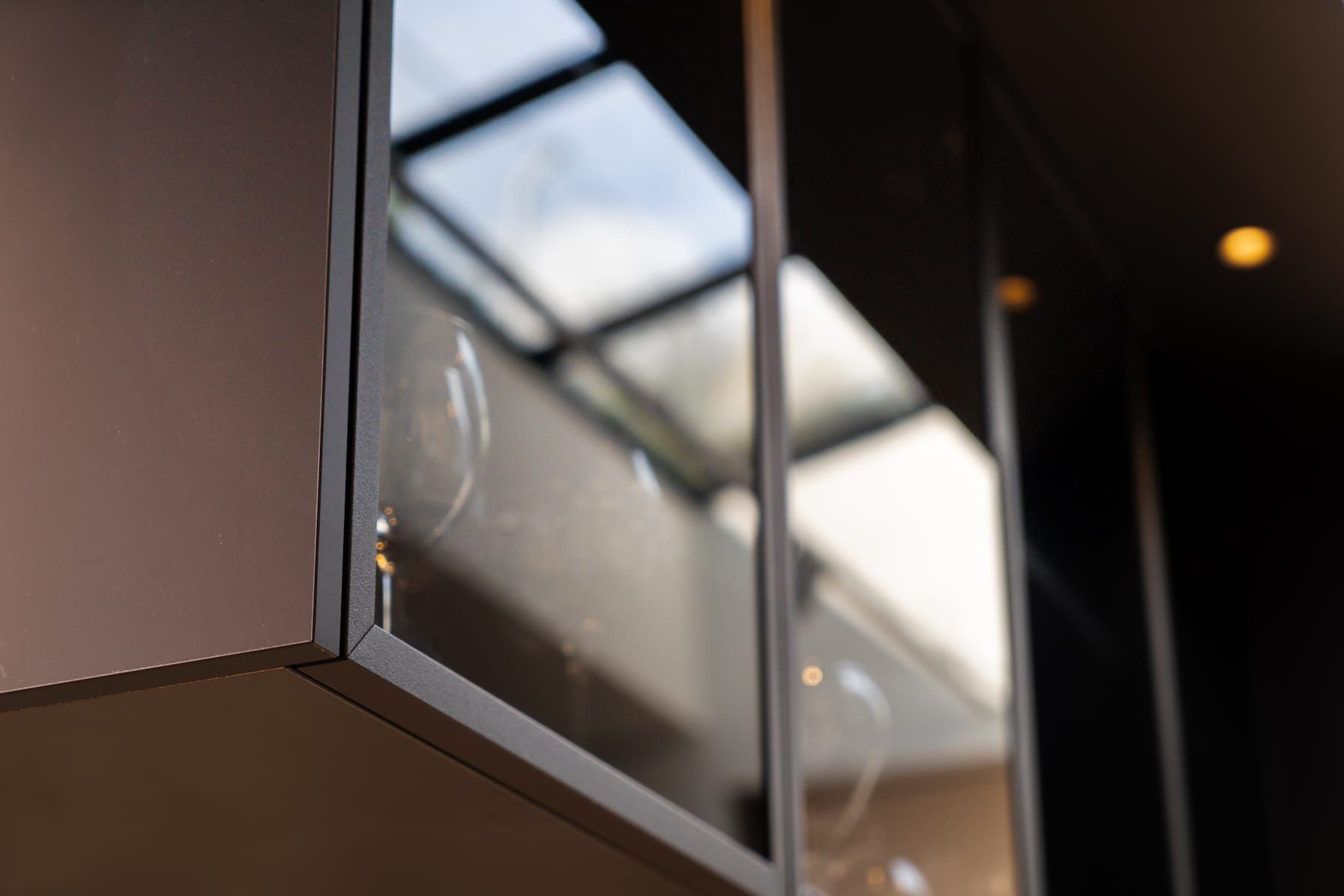 Black framed glass cabinet reflecting the skylight above the kitchen