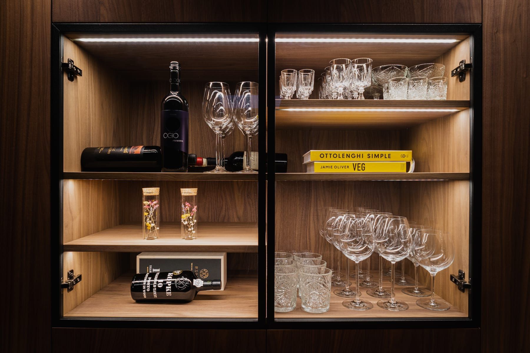 Glass display cabinet with lit wood shelves holding glasses and bottles