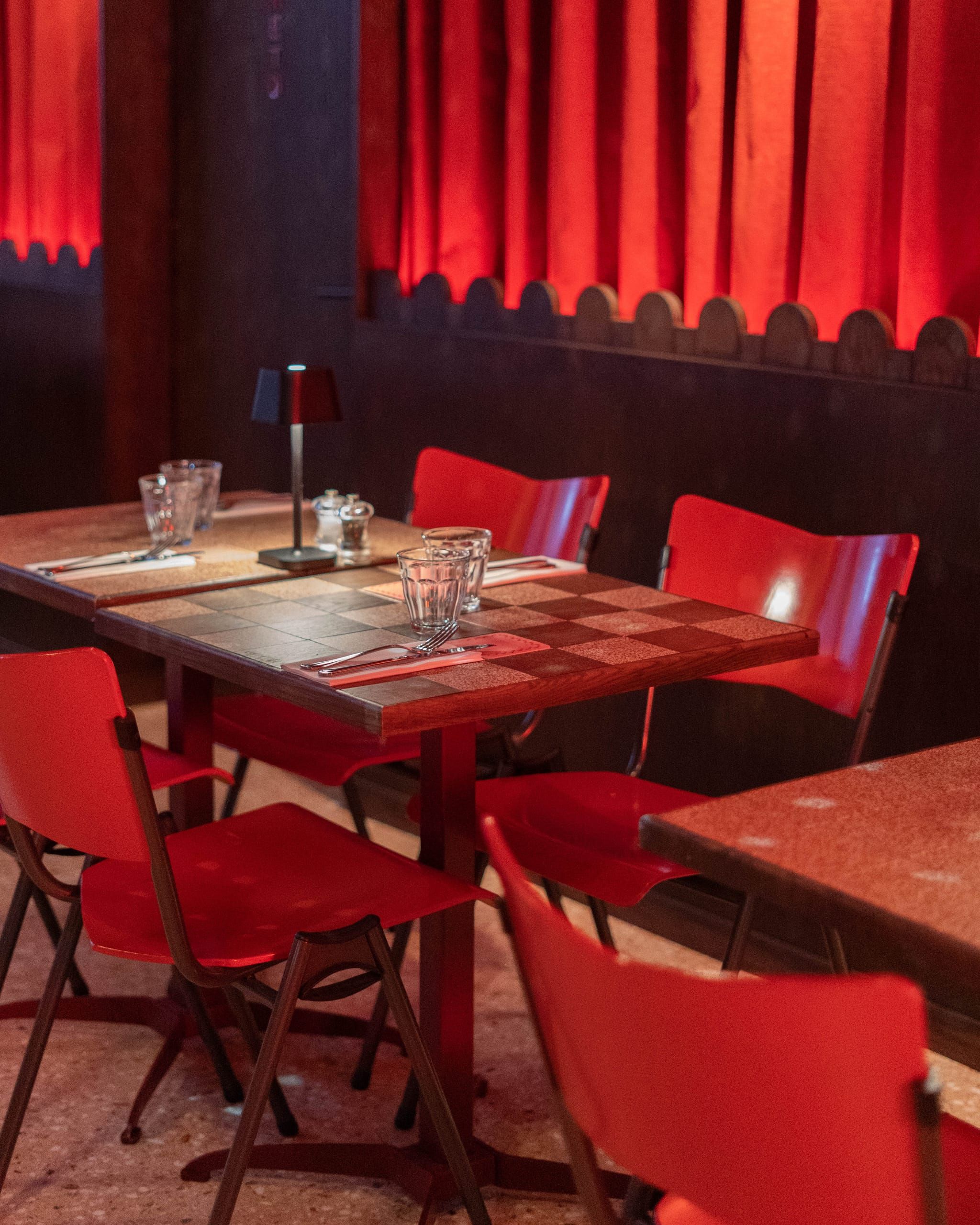 Dark wood panelling and red curtains behind small tables and red chairs