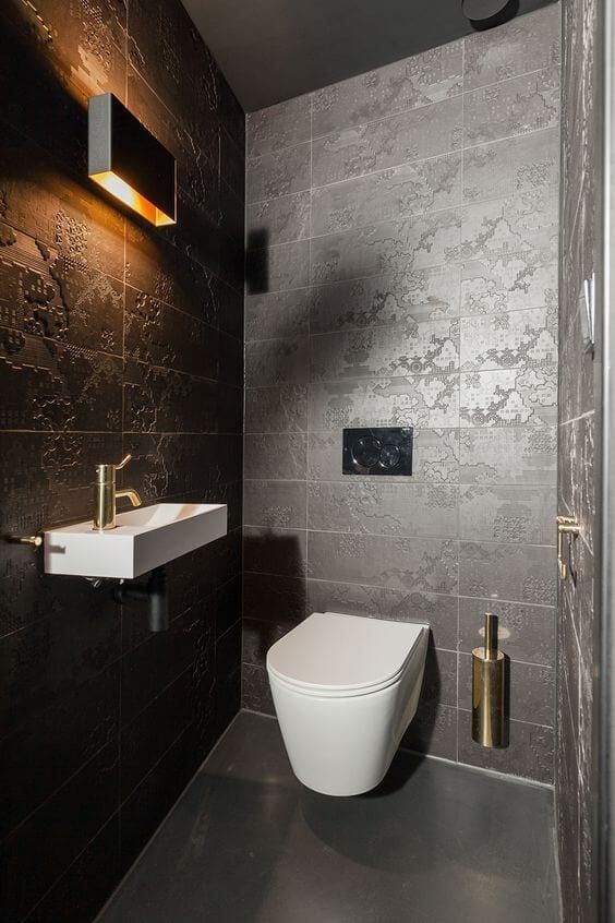 Dark cloakroom with patterned tiles, brass tap and a wall light
