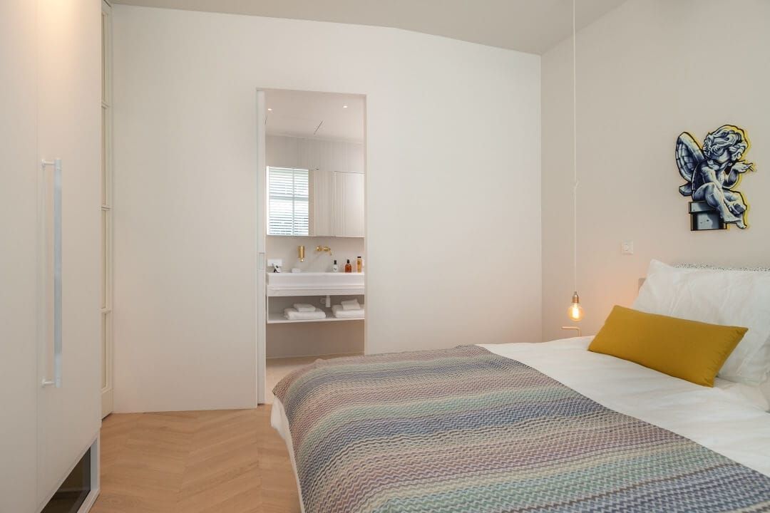 Bedroom with herringbone floor, pendant bulb and an open door to the bathroom