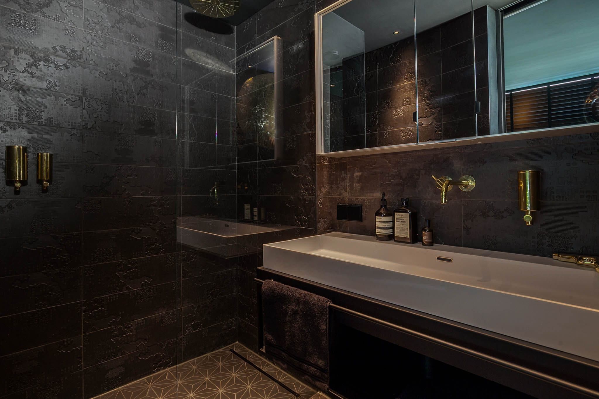 Dark bathroom with glass shower, long basin and brass fittings in Moonlight
