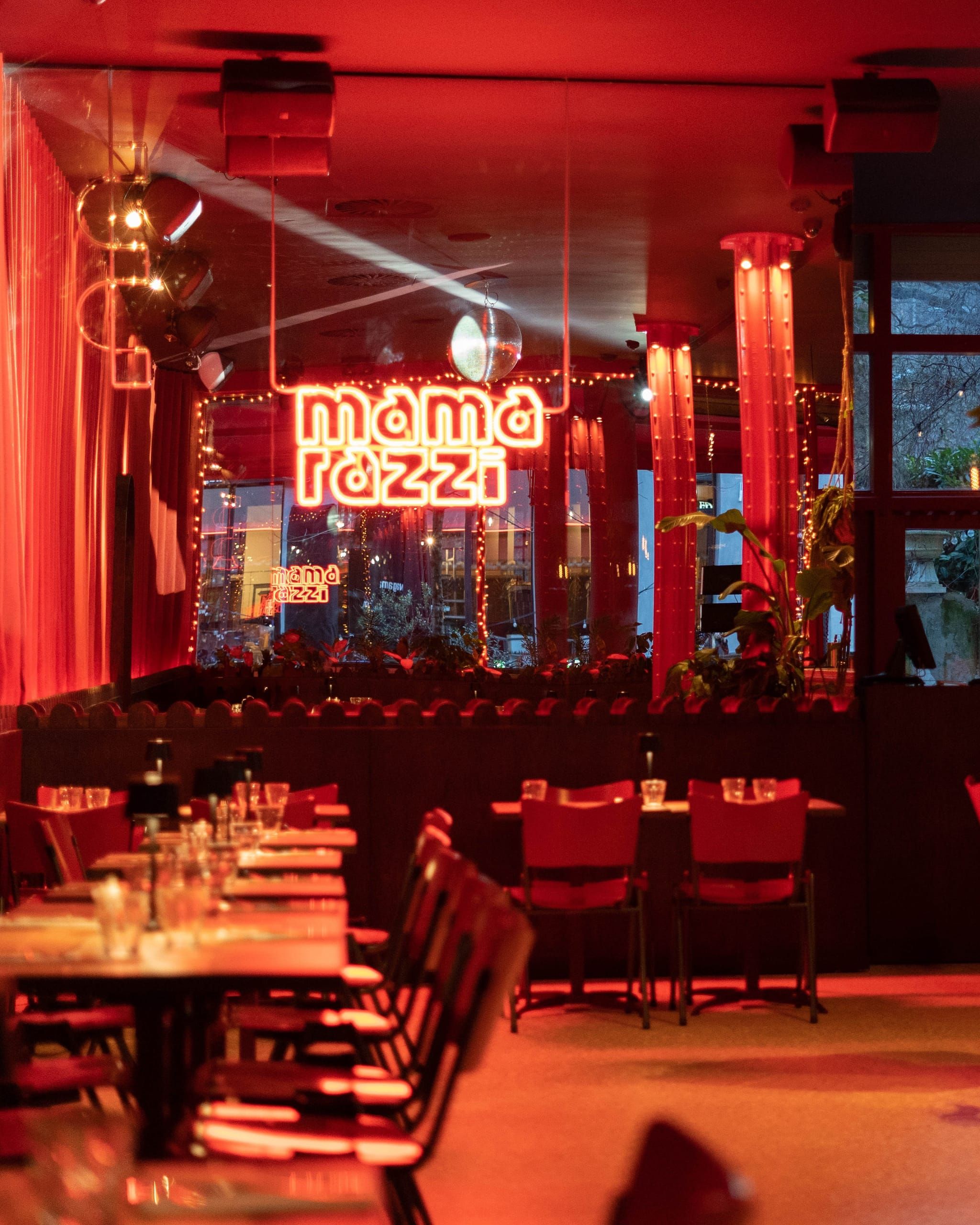 Neon Mamarazzi sign above rows of tables in the red-lit restaurant
