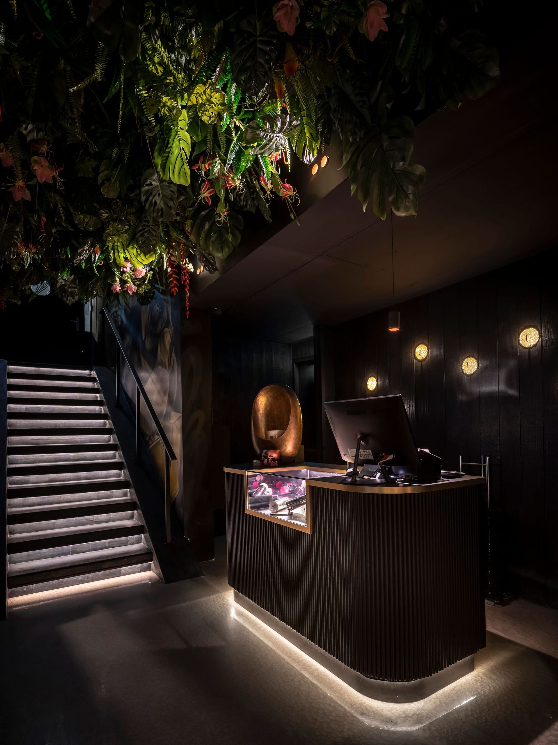 Entrance desk with fluted front and glowing base beside a lit staircase at Vandal