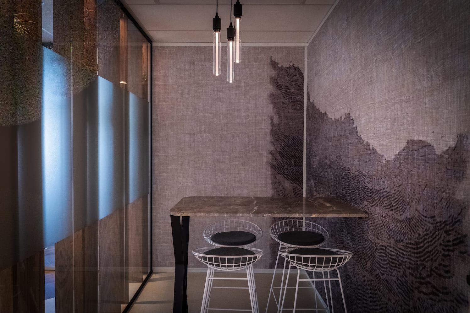 Small meeting nook with a marble high table, wire stools and patterned wallpaper