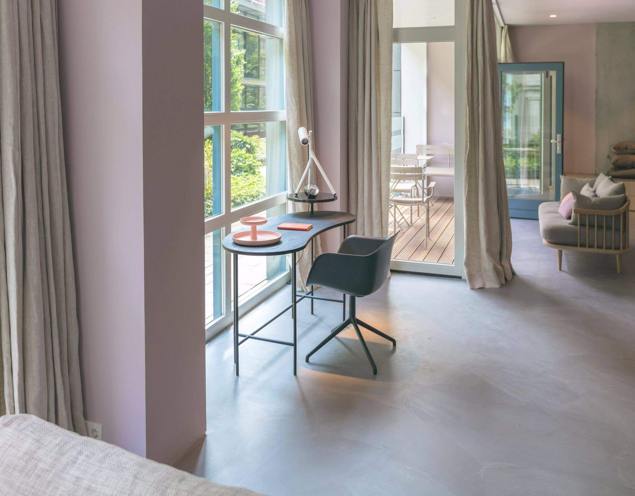 Curved desk and grey chair by tall windows and a terrace door