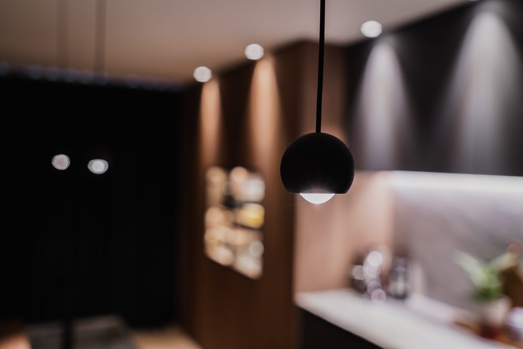 Black pendant light with blurred walnut cabinet wall behind in Churchlane