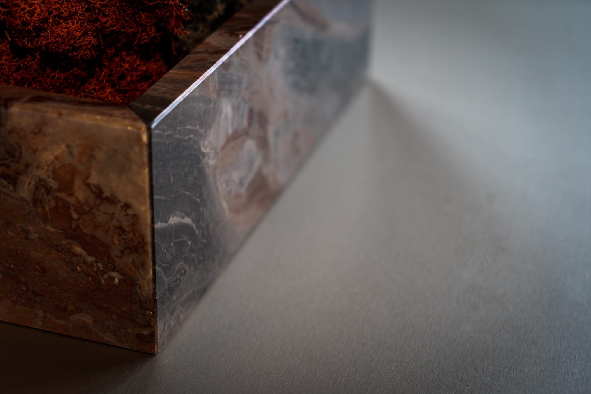 Detail of a marble planter box with red moss on a grey surface