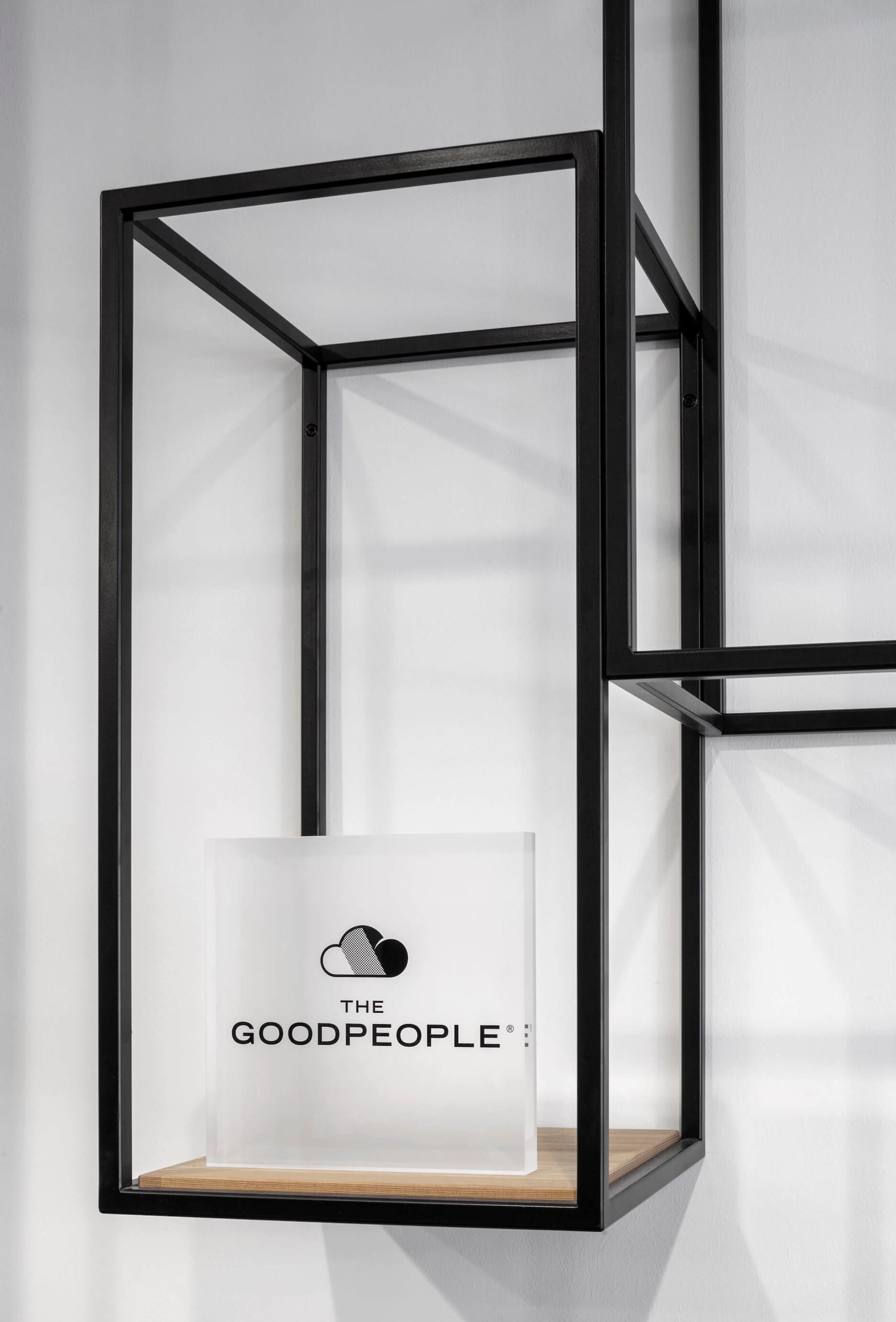 Black steel frame shelf holding a frosted acrylic logo block against a white wall