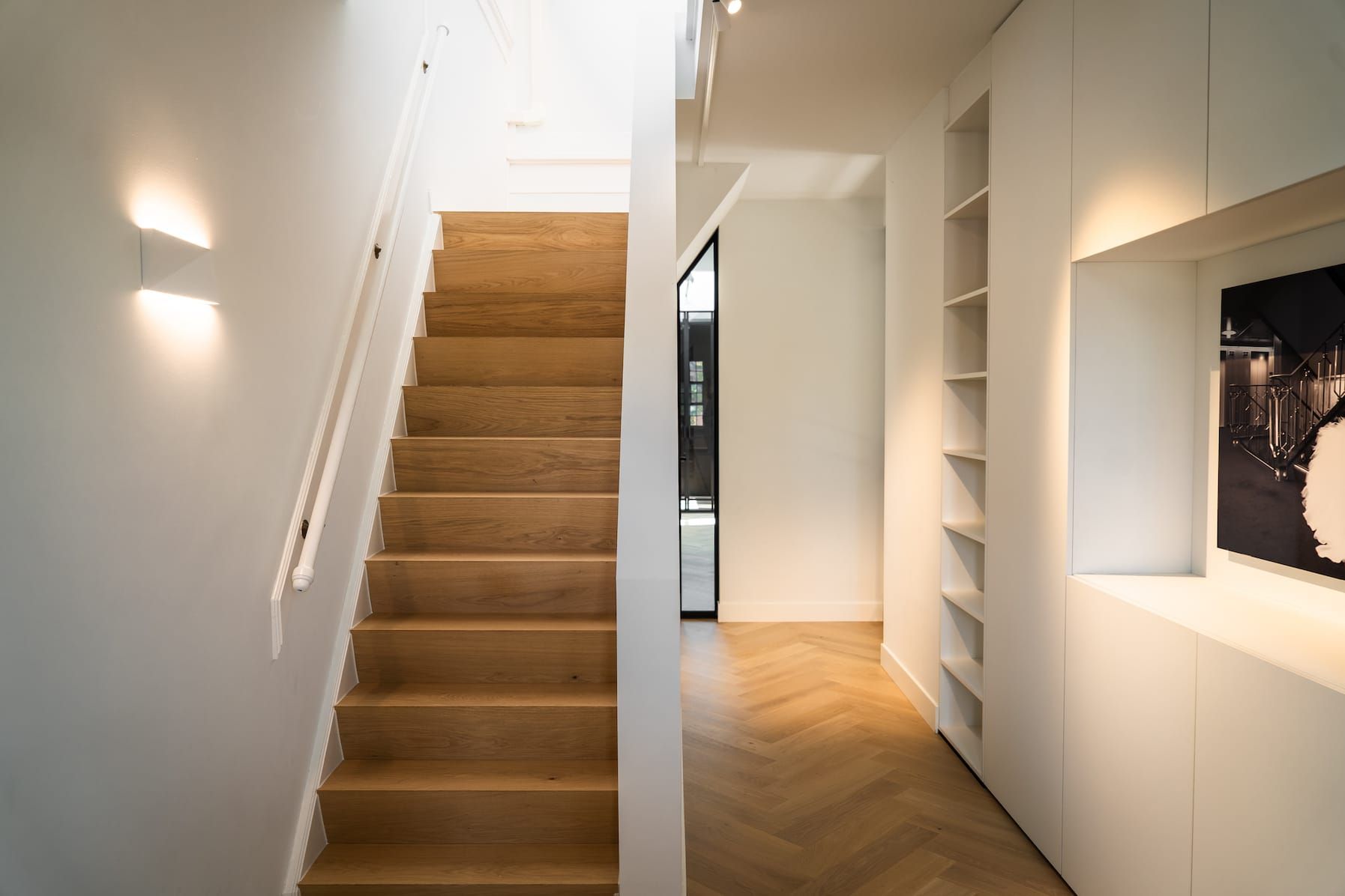 Oak staircase with white wall light and built-in white cabinetry in the hallway