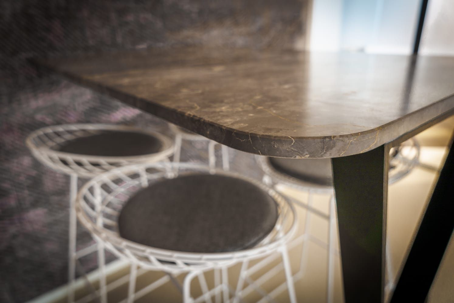 Close-up of a rounded marble tabletop above white wire stools with dark seats