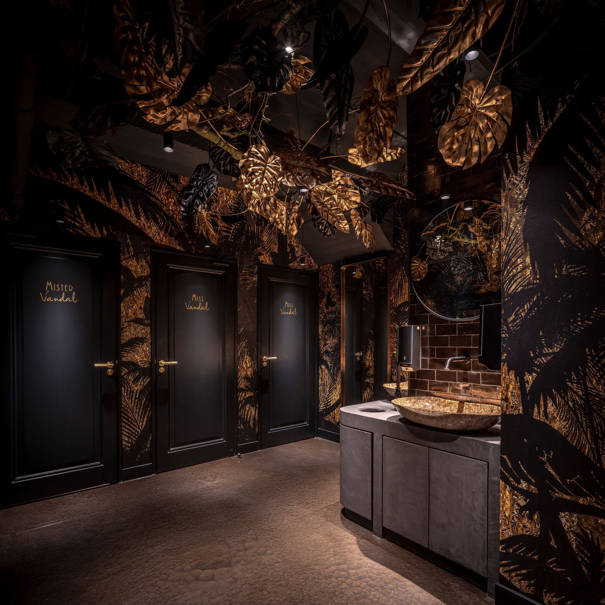 Restroom corridor with black doors, gold leaf wallpaper and a gold basin at Vandal