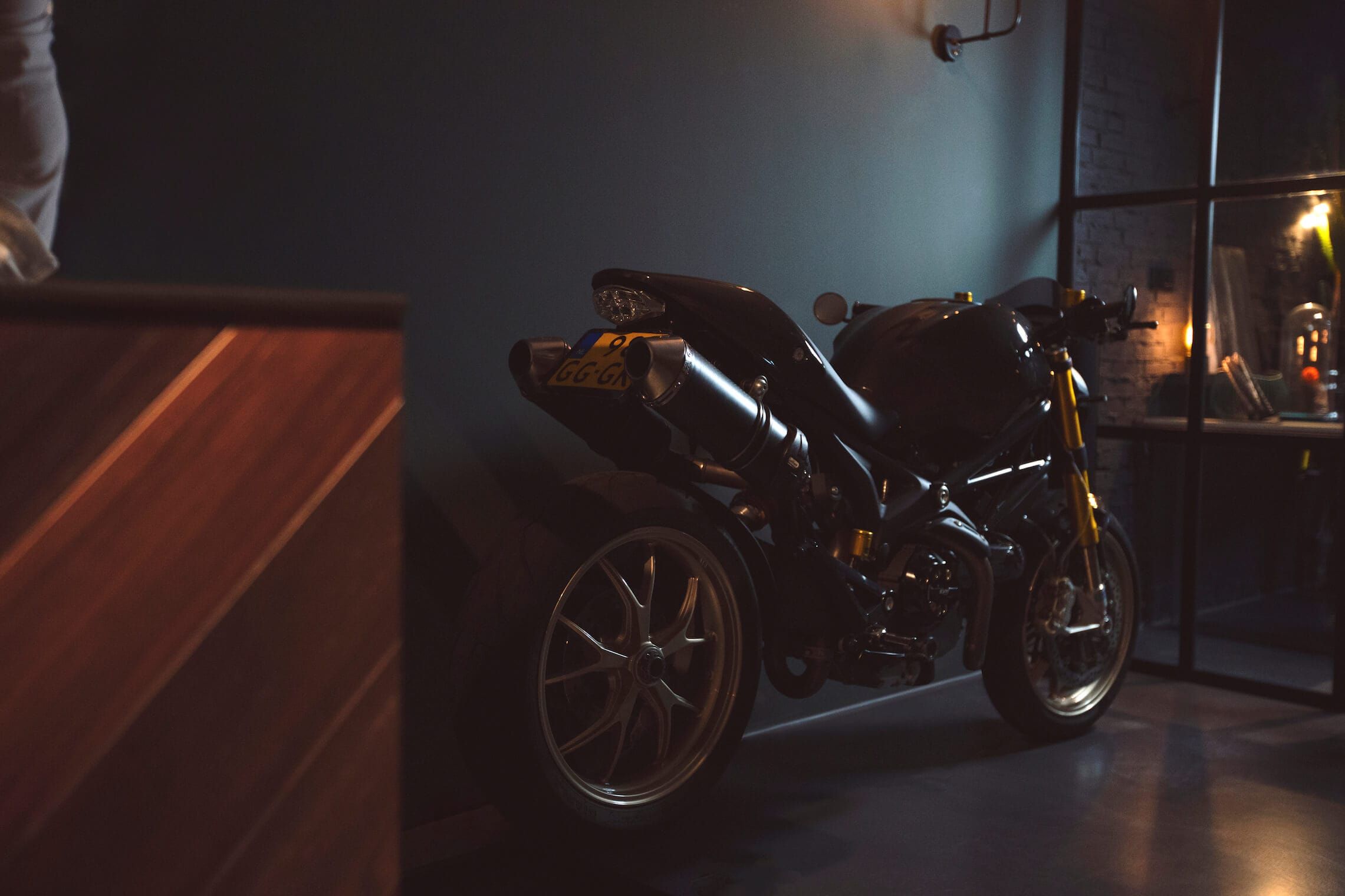 Motorbike parked against a dark teal wall beside a walnut cabinet front