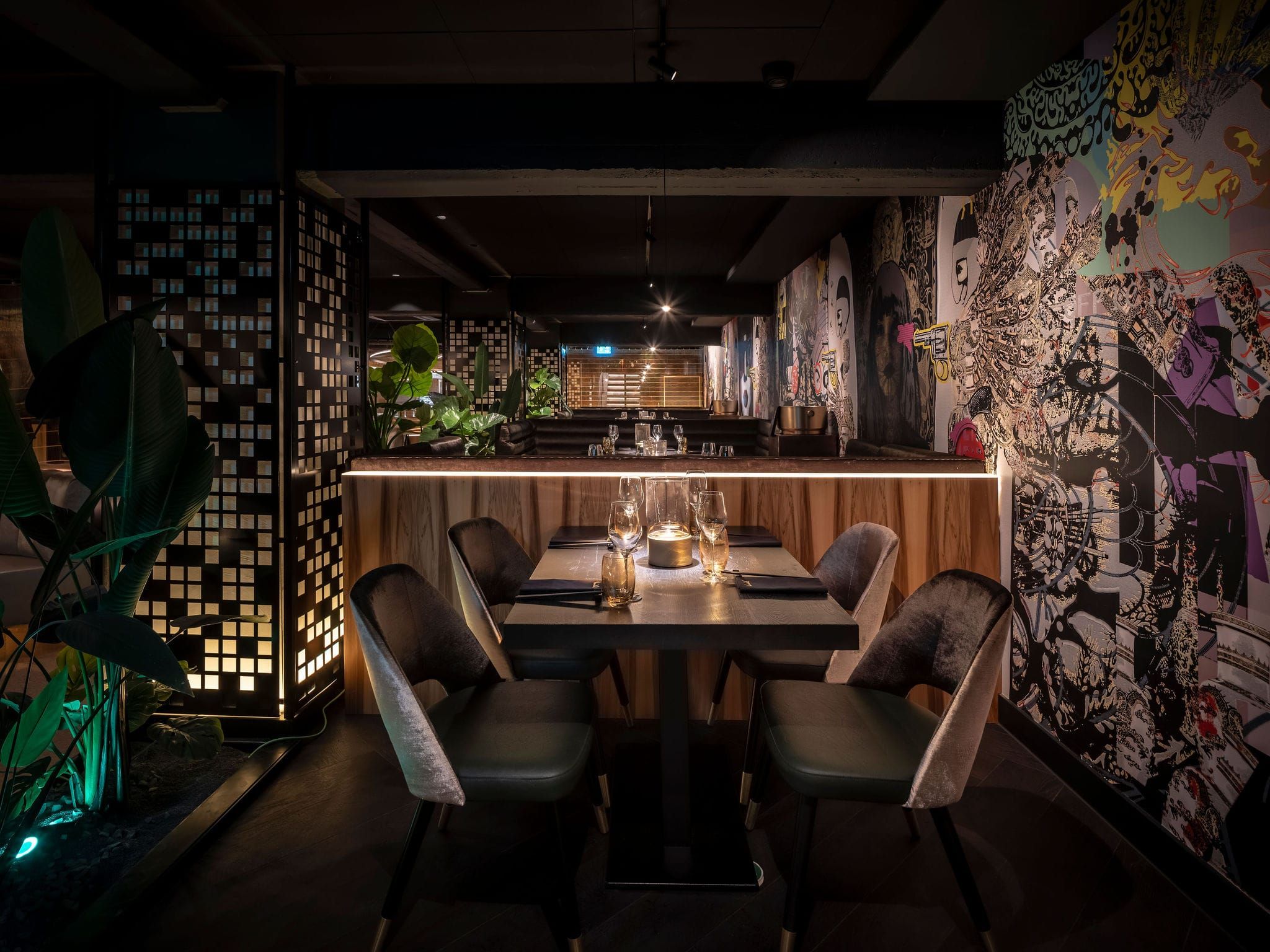 Table for four with velvet chairs, backlit mosaic screen and mural wall at Vandal