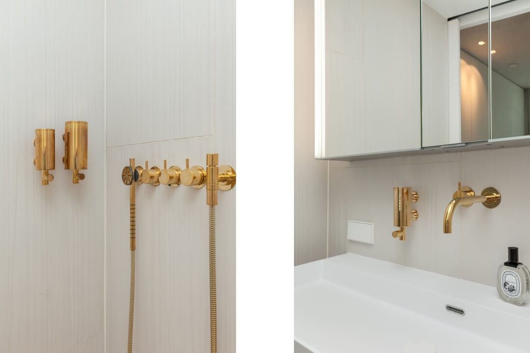 Brass shower fittings and soap dispensers beside a basin with mirror cabinet