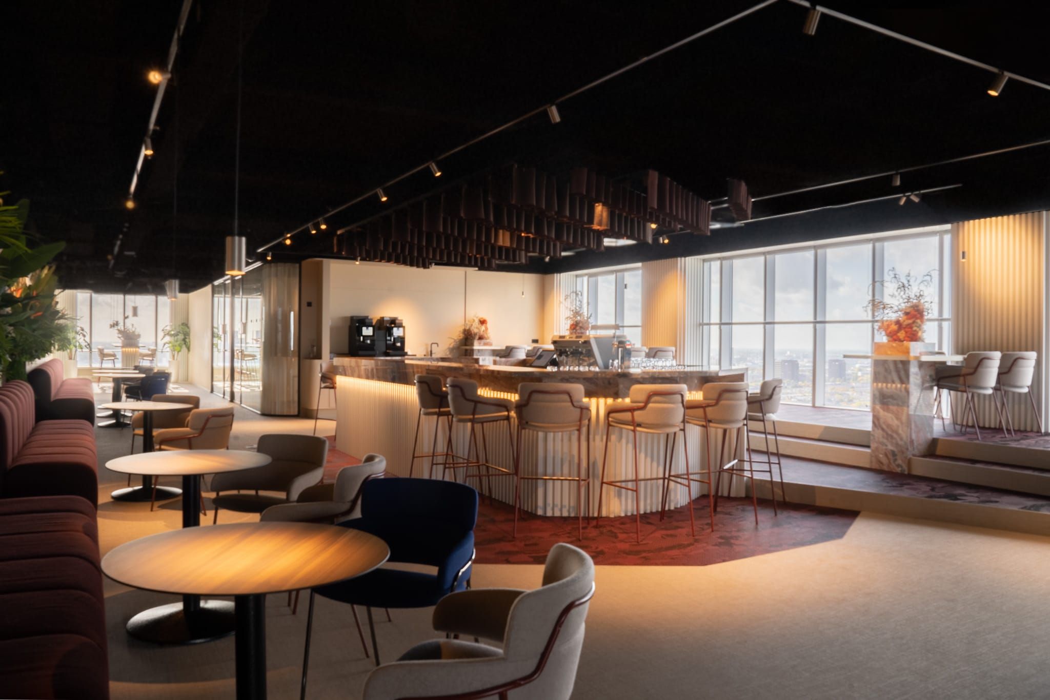 Open lounge with bar, burgundy banquettes and stools under a dark ceiling